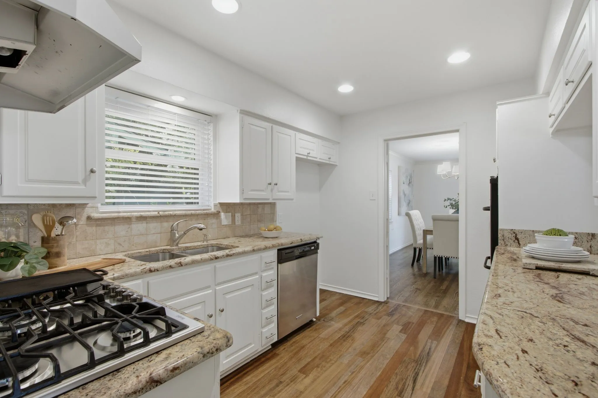 Kitchen featuring white cabinetry, granite countertops, tile backsplash, stainless steel appliances, and wood-finish flooring