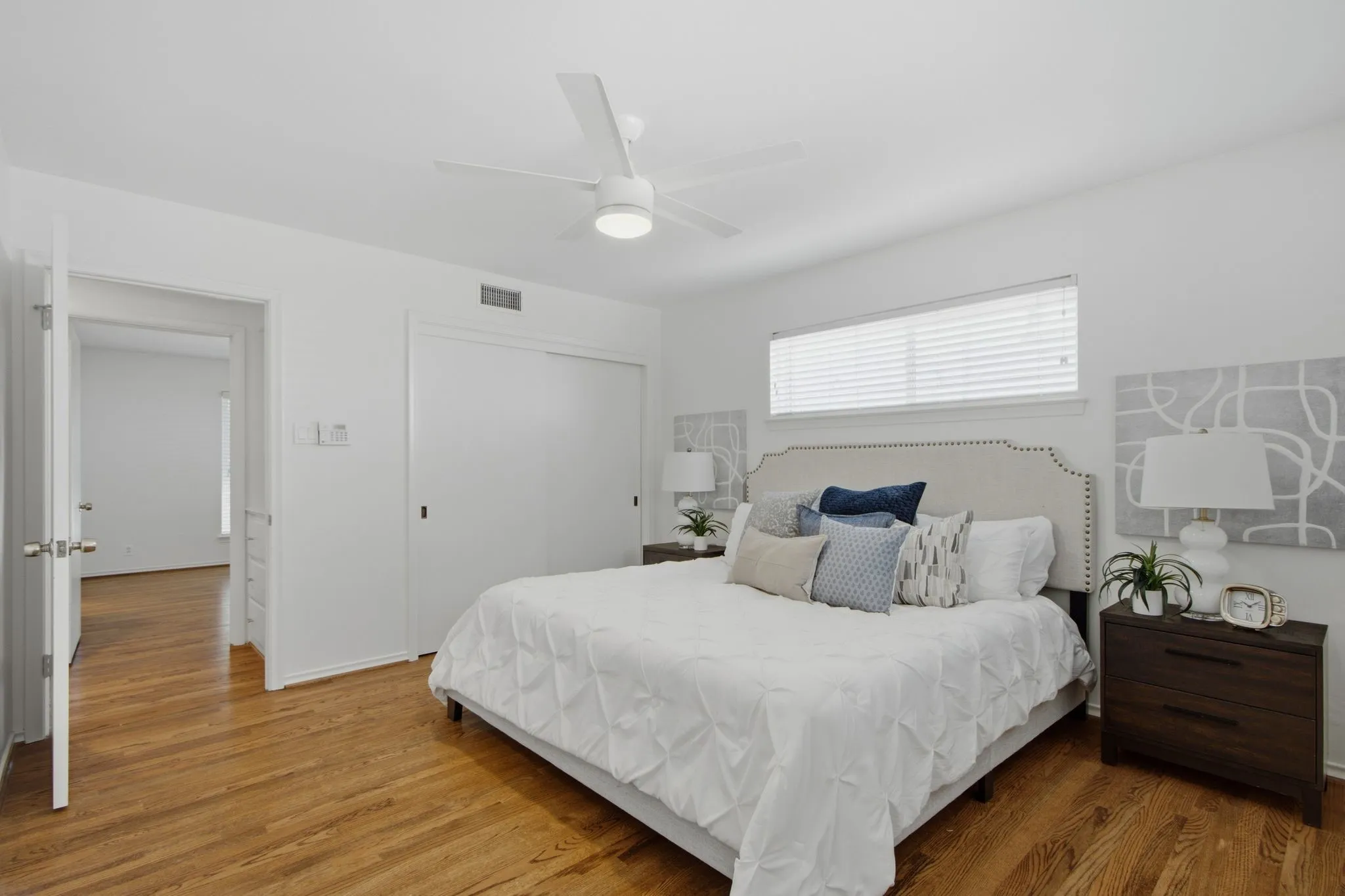 Spacious room featuring wood-finish flooring, a ceiling fan with integrated lighting, and a wide window with blinds
