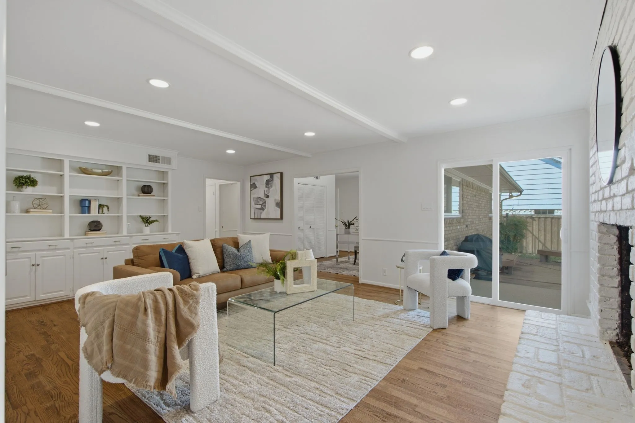 Spacious living area featuring wood-finish flooring, built-in shelving with lower cabinetry, a white brick fireplace, recessed lighting, and a sliding glass door