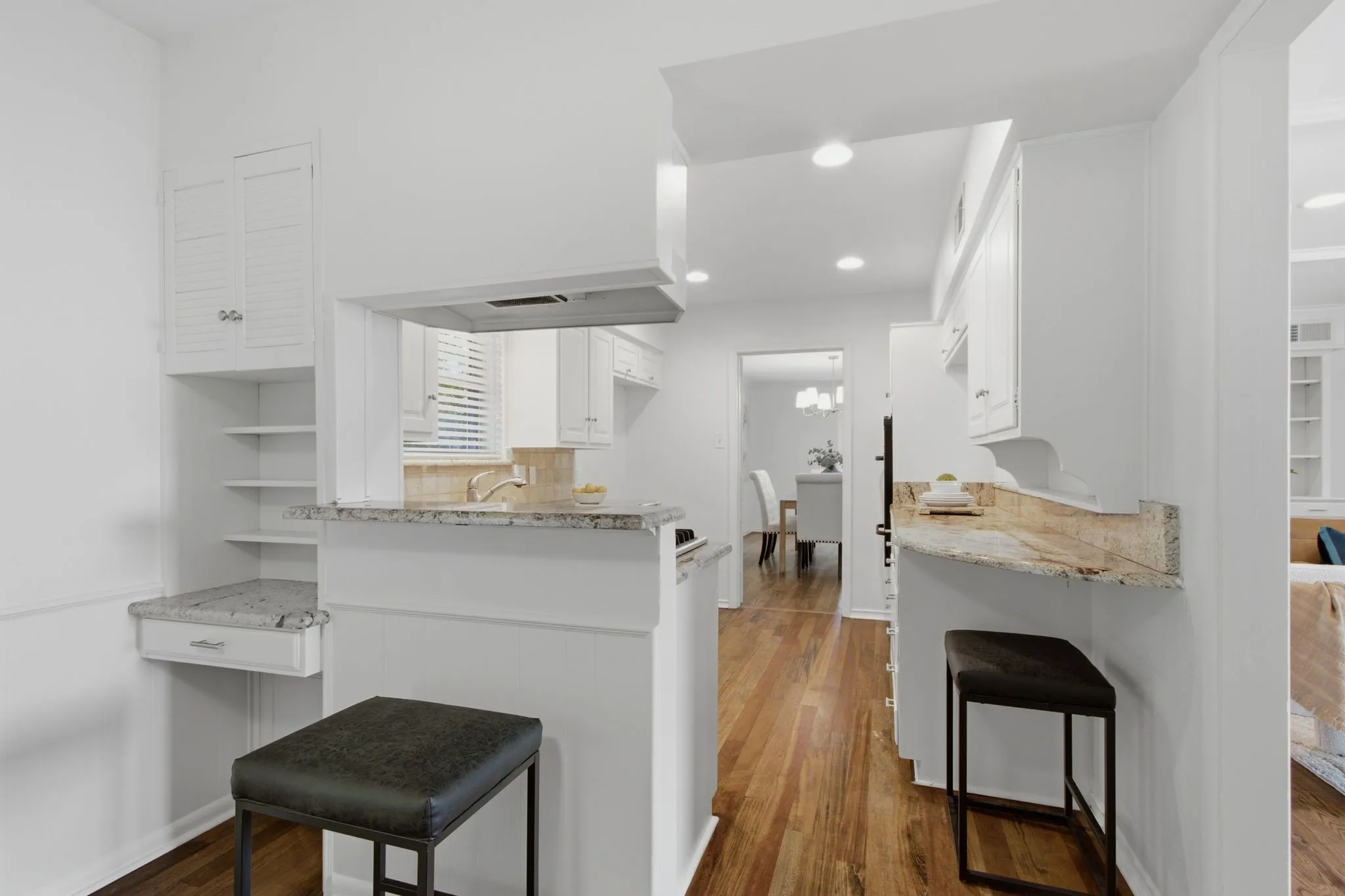Kitchen featuring white cabinetry, granite countertops, wood-finish flooring, and a pass-through window with a breakfast bar