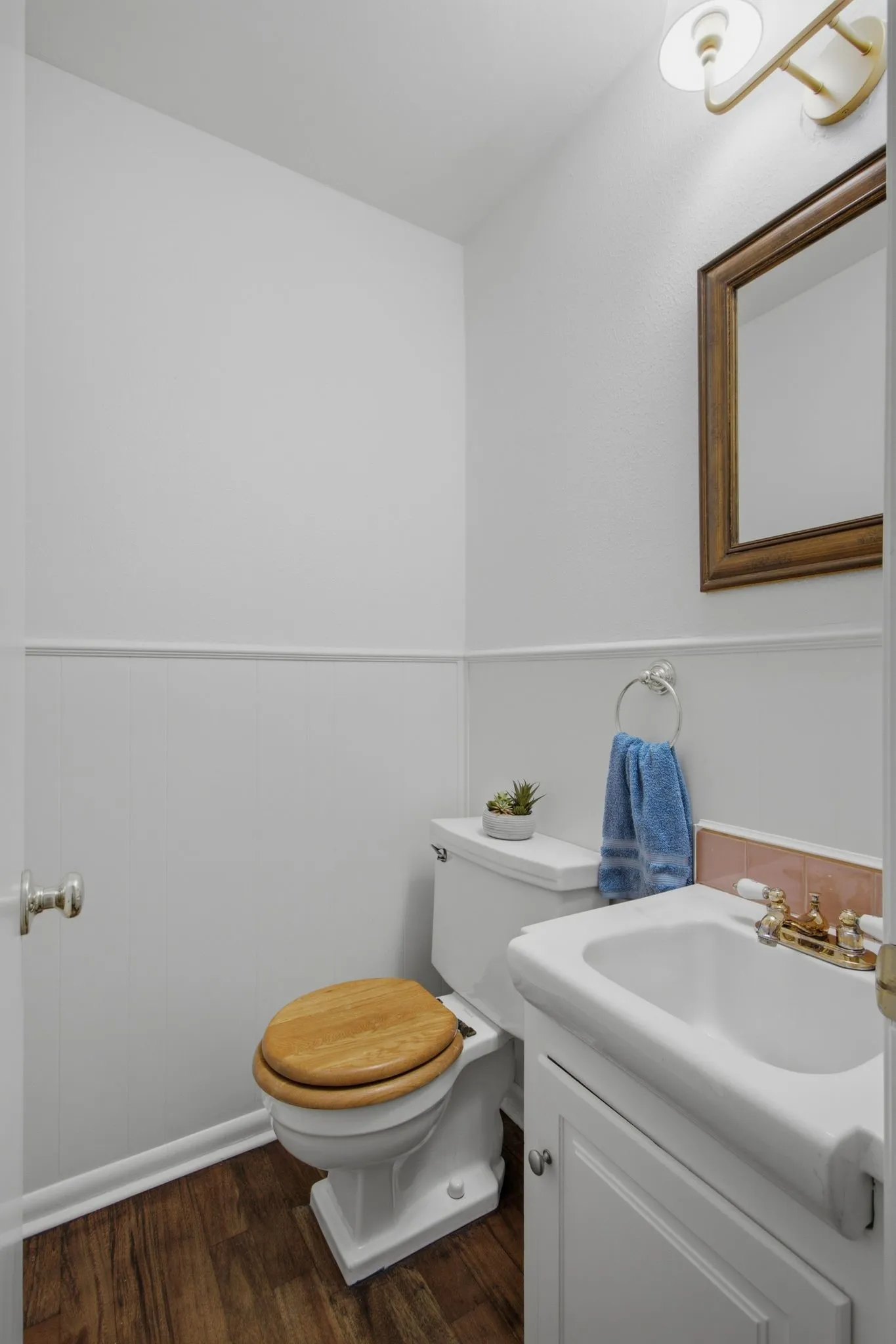 Compact powder room featuring wood-finish flooring, wainscoting, and a white vanity with an integrated sink