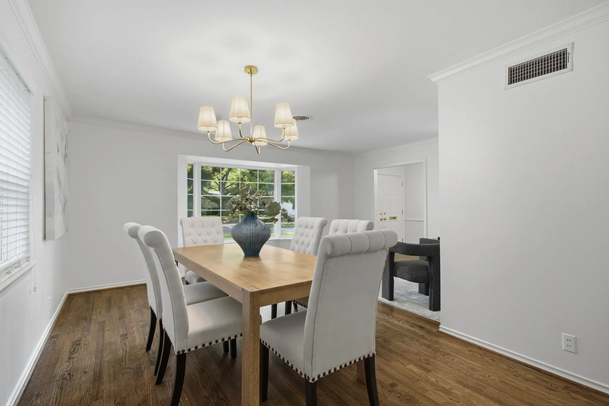 Dining area featuring wood-finish flooring, a contemporary chandelier, a large bay window, white crown molding, and a neutral color palette