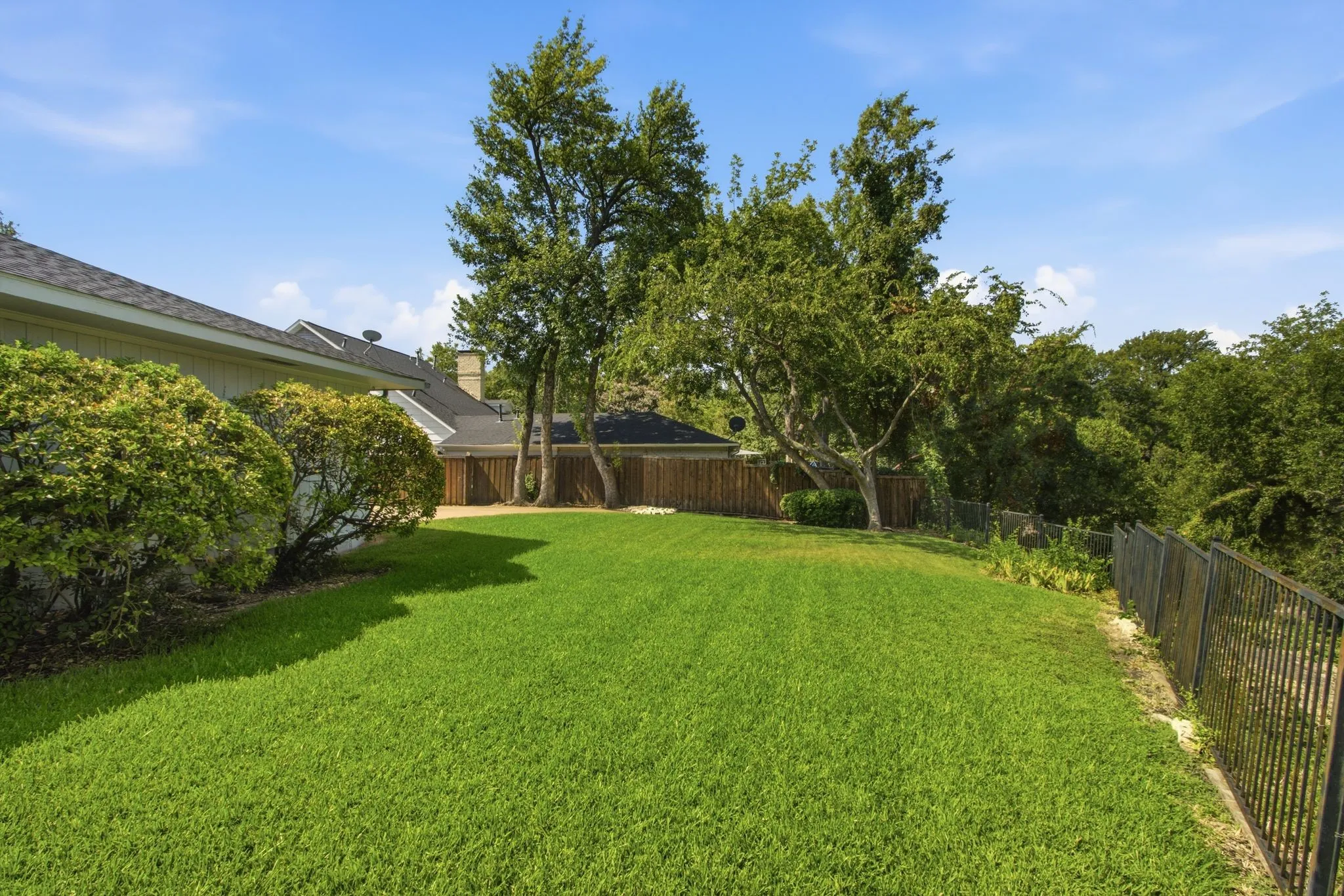 Expansive green lawn with mature trees and established perimeter landscaping