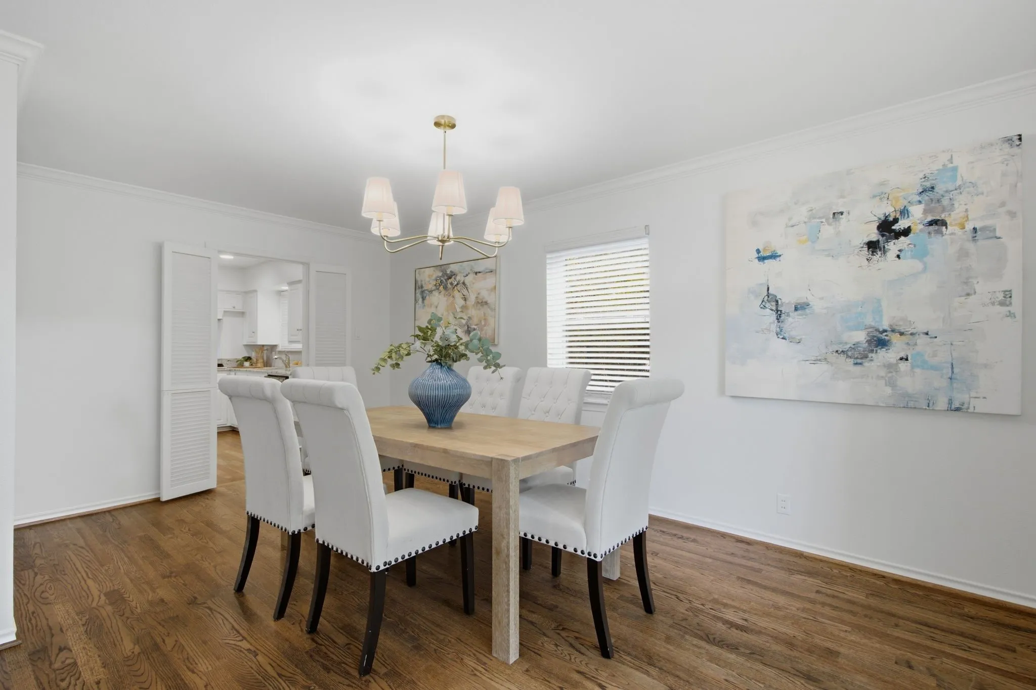 Dining area featuring rich wood-finish flooring, white walls, and a brass chandelier with fabric shades