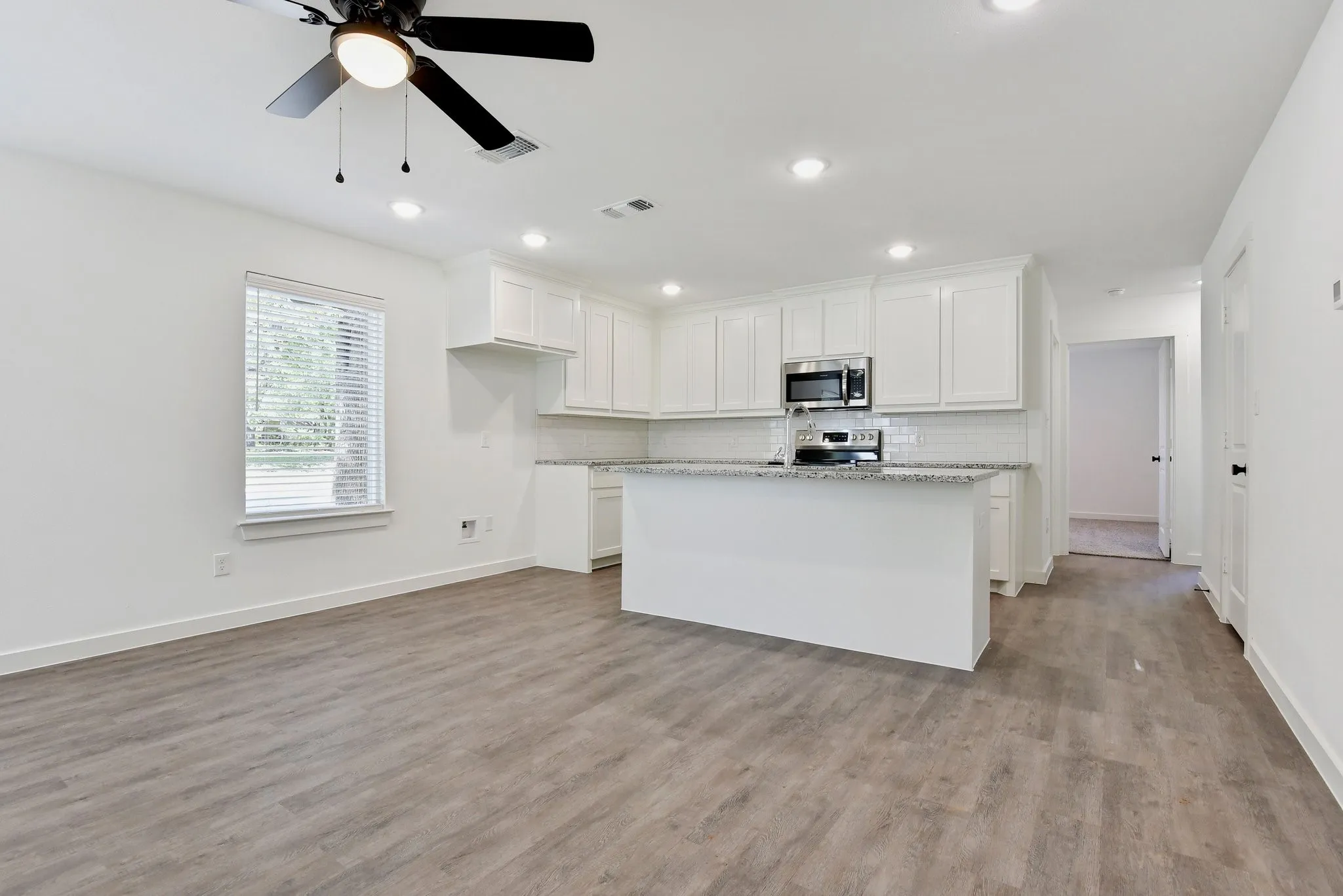 Kitchen featuring white cabinetry, a center island with sink, backsplash, light wood-style floors, and recessed lighting