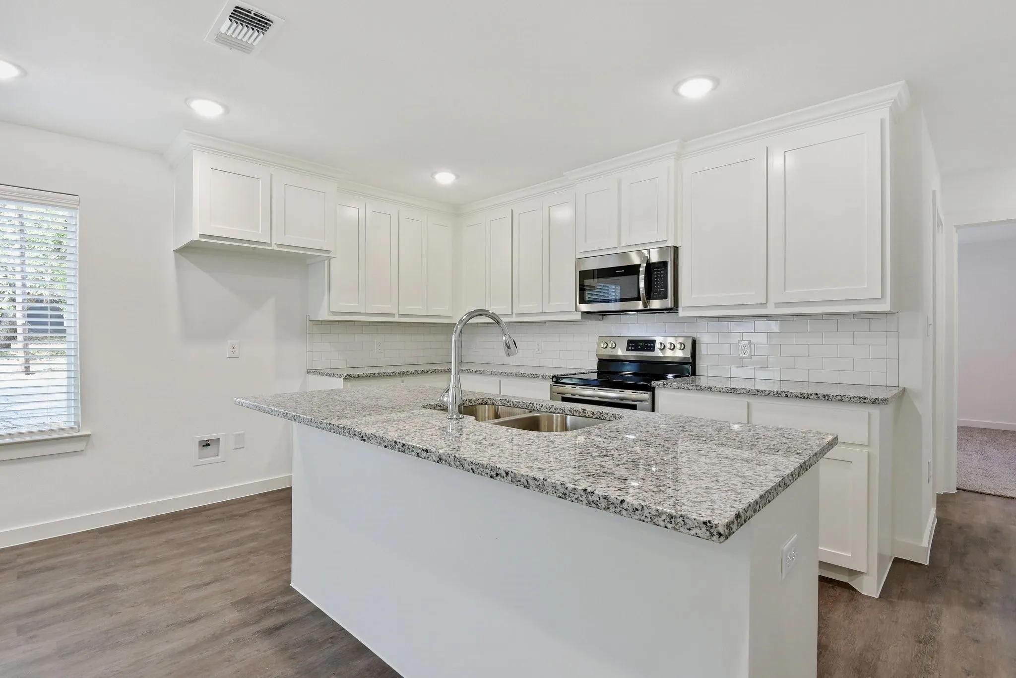 Kitchen featuring white cabinets, appliances with stainless steel finishes, light stone counters, tasteful backsplash, and a center island with sink