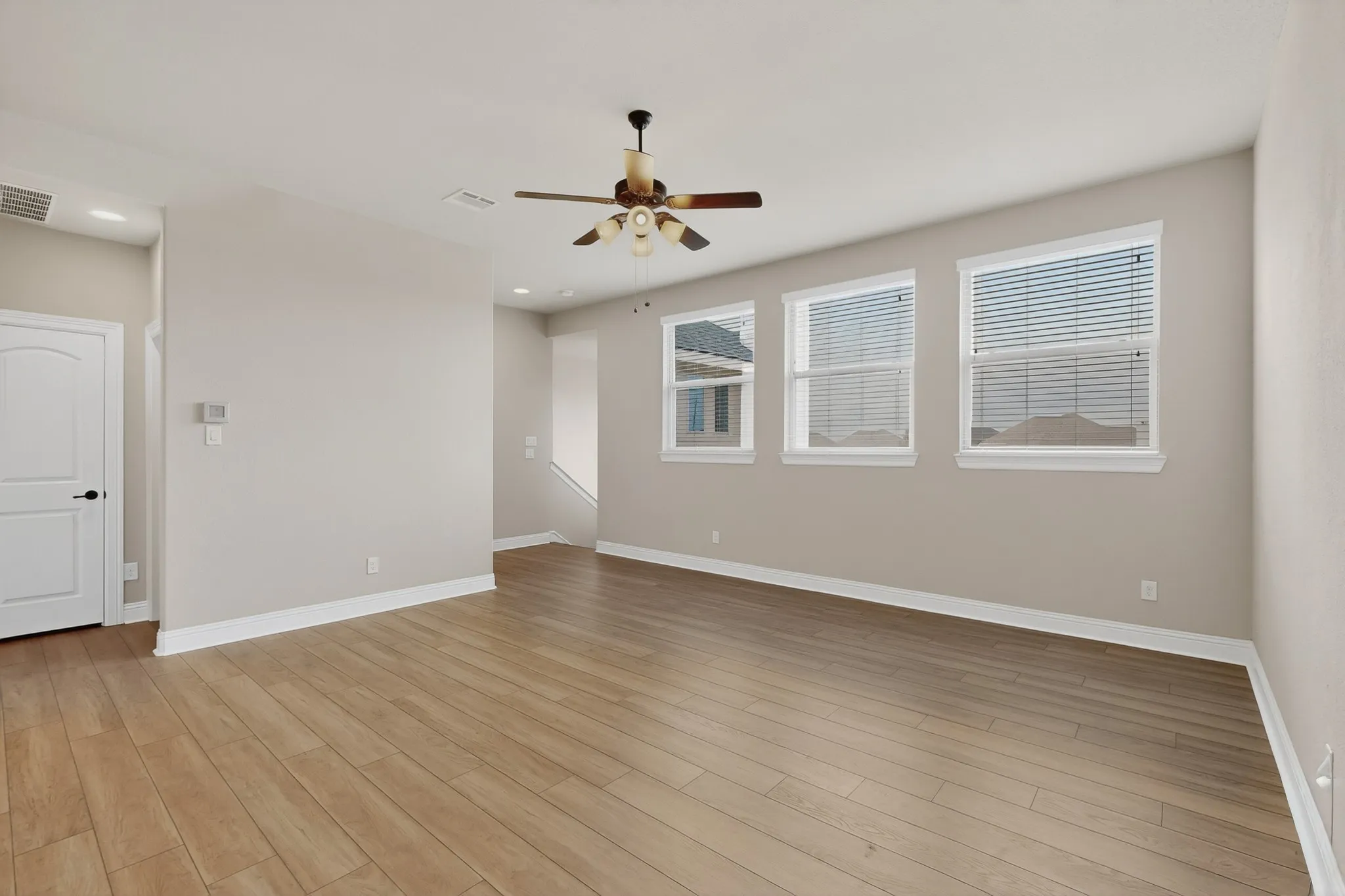 Spacious living area on 2nd floor showcasing wood-finish flooring throughout, abundant natural light from multiple windows, ceiling fan with integrated lighting, and neutral wall finishes providing a versatile backdrop for any décor