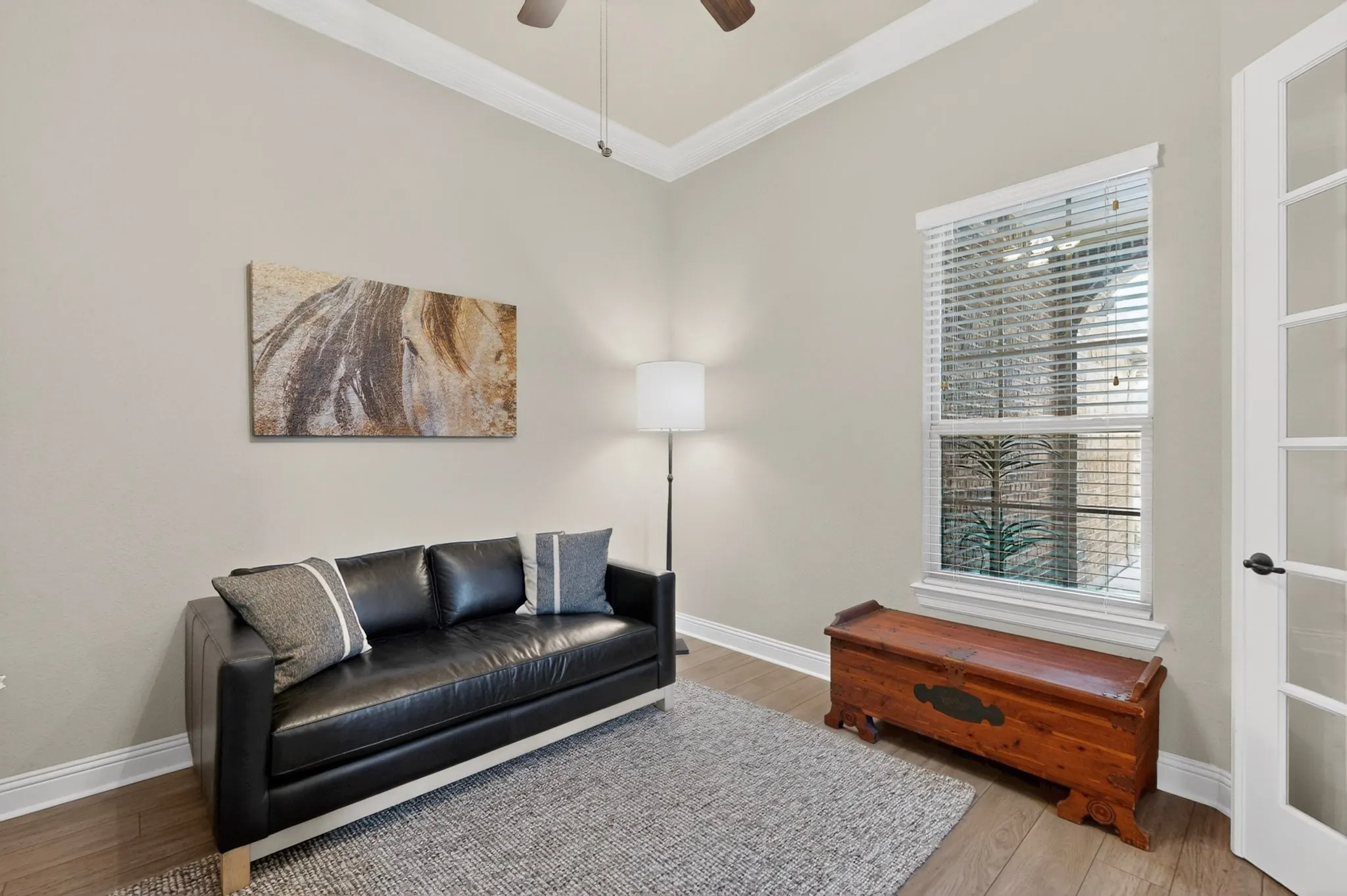 Bright, light-filled room featuring hardwood flooring, a ceiling fan, and plantation shutters