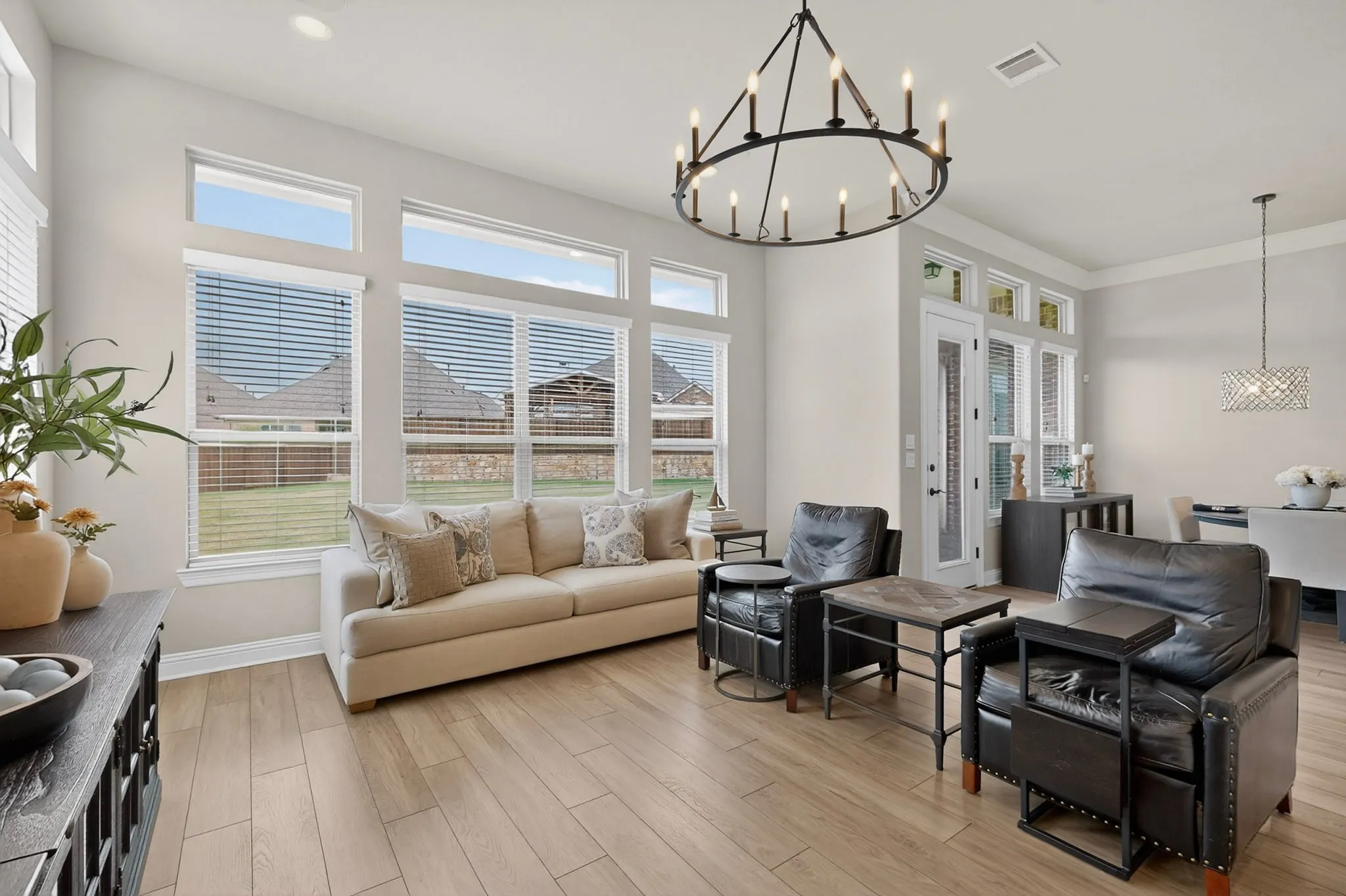 Bright open-concept living area showcasing expansive windows with integrated blinds, light wood-finish flooring throughout, and a coffered ceiling with decorative pendant lighting