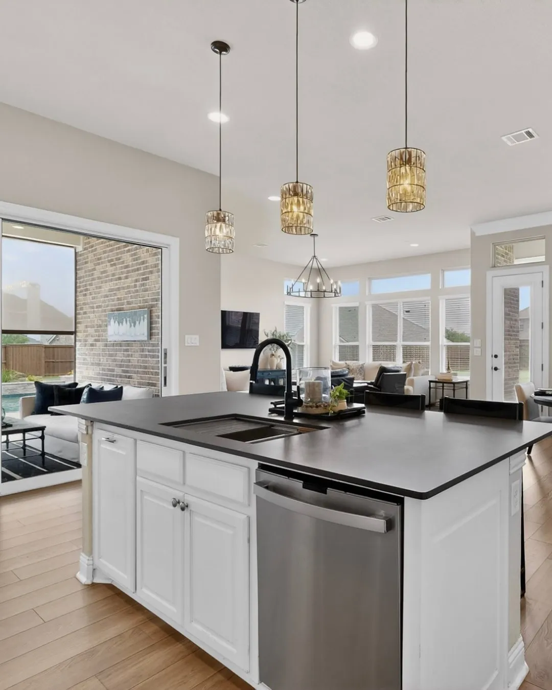 Kitchen island with a dark countertop and integrated sink, stainless steel dishwasher, white cabinetry, and wood-finish flooring