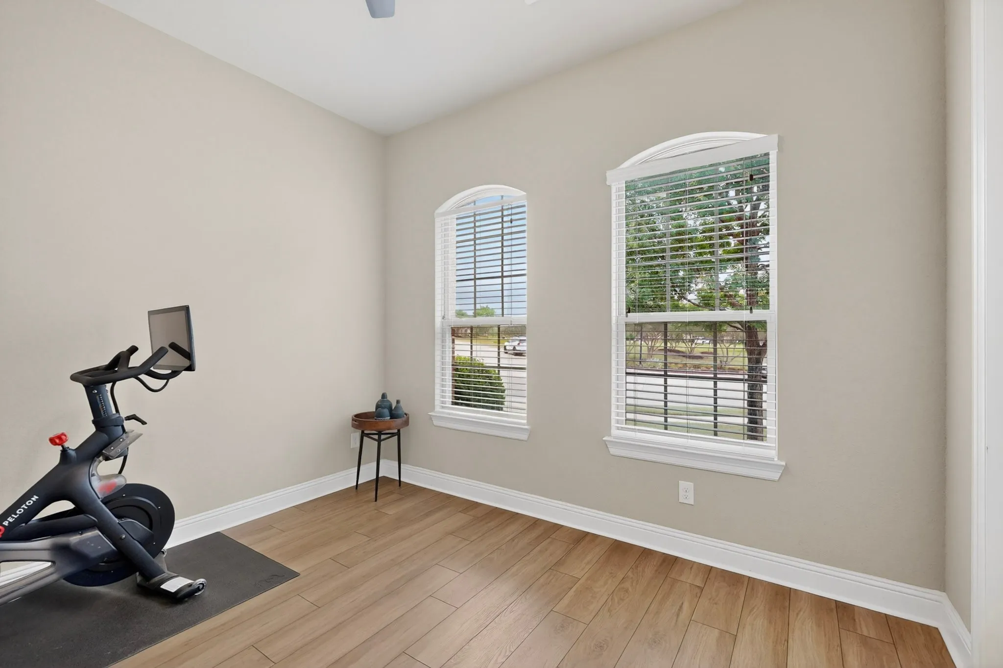 Bright home gym featuring arched windows with plantation shutters, hardwood flooring, and natural light
