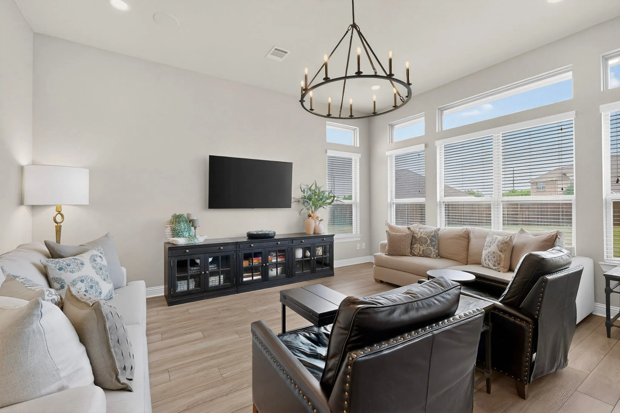 Spacious living area featuring high ceilings, wood-finish flooring, a large circular chandelier, and extensive fenestration with horizontal blinds