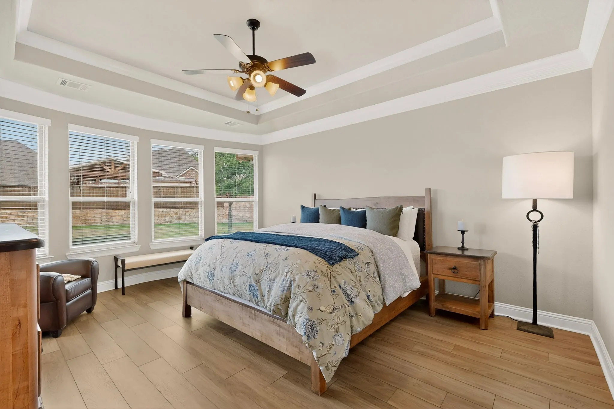 Spacious primary bedroom showcasing a coffered ceiling with recessed lighting, ceiling fan with integrated light fixture, and abundant natural light from multi-pane windows overlooking the exterior landscape