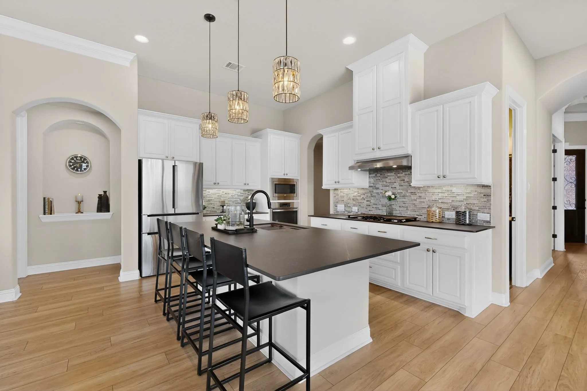 Chef's kitchen featuring white cabinetry, stainless steel appliances, a large center island with black countertop seating, pendant lighting, subway tile backsplash, and wood-finish flooring throughout the open-concept space