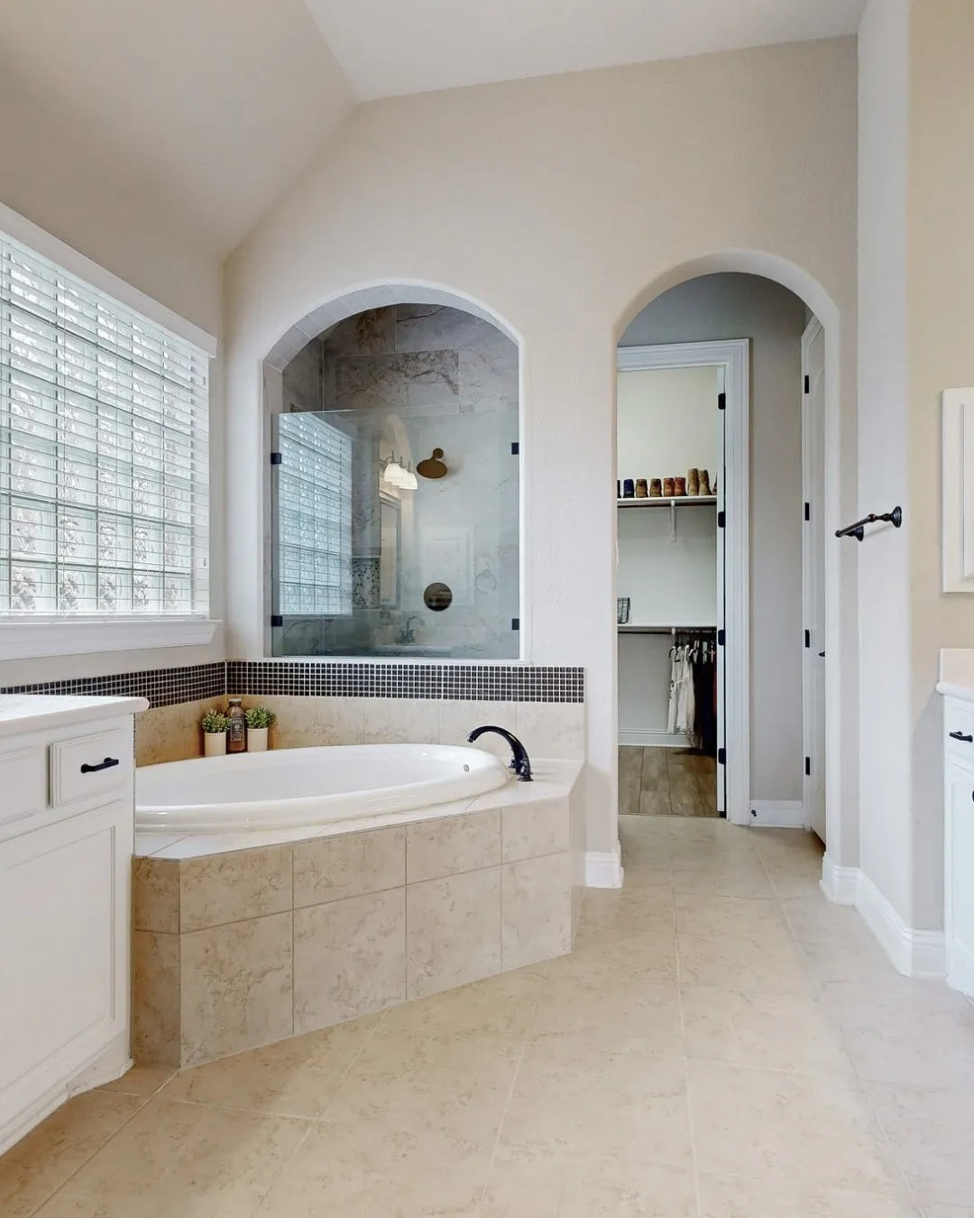 Arched doorways, tiled flooring, built-in soaking tub, glass-enclosed shower, and a vaulted ceiling