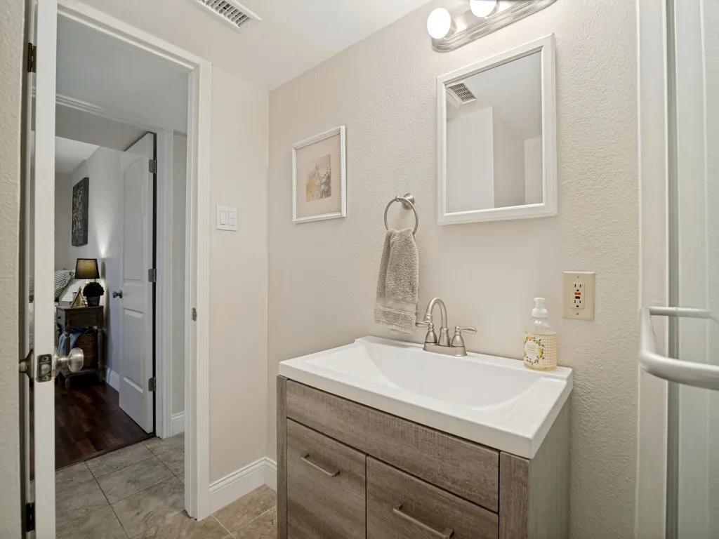 Full bathroom located in the hallway off the kitchen and secondary bedrooms, with access to a back door off the patio.