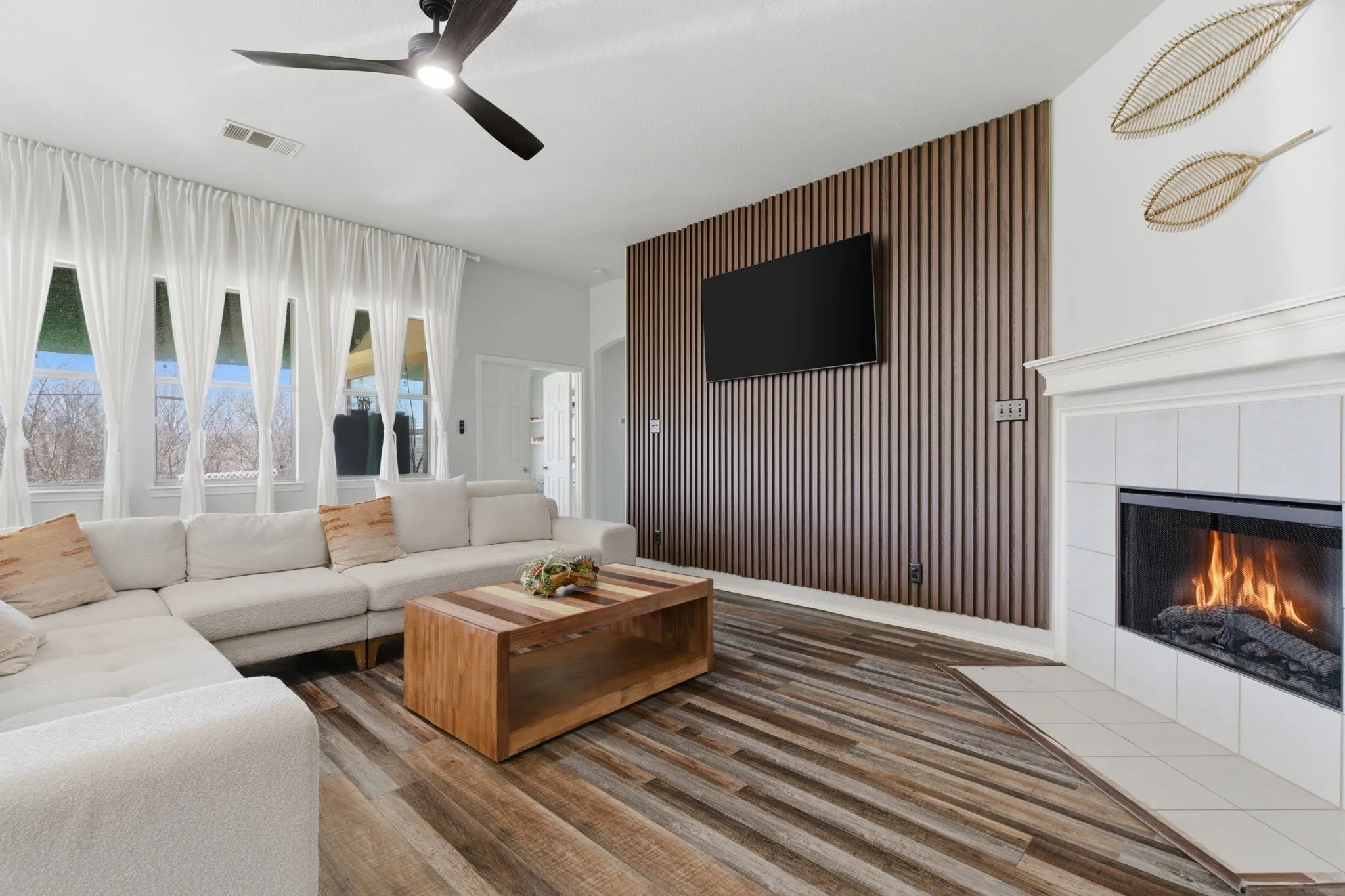 Living area featuring wood-finish flooring, a white tiled fireplace with a mantel, and a slatted accent wall