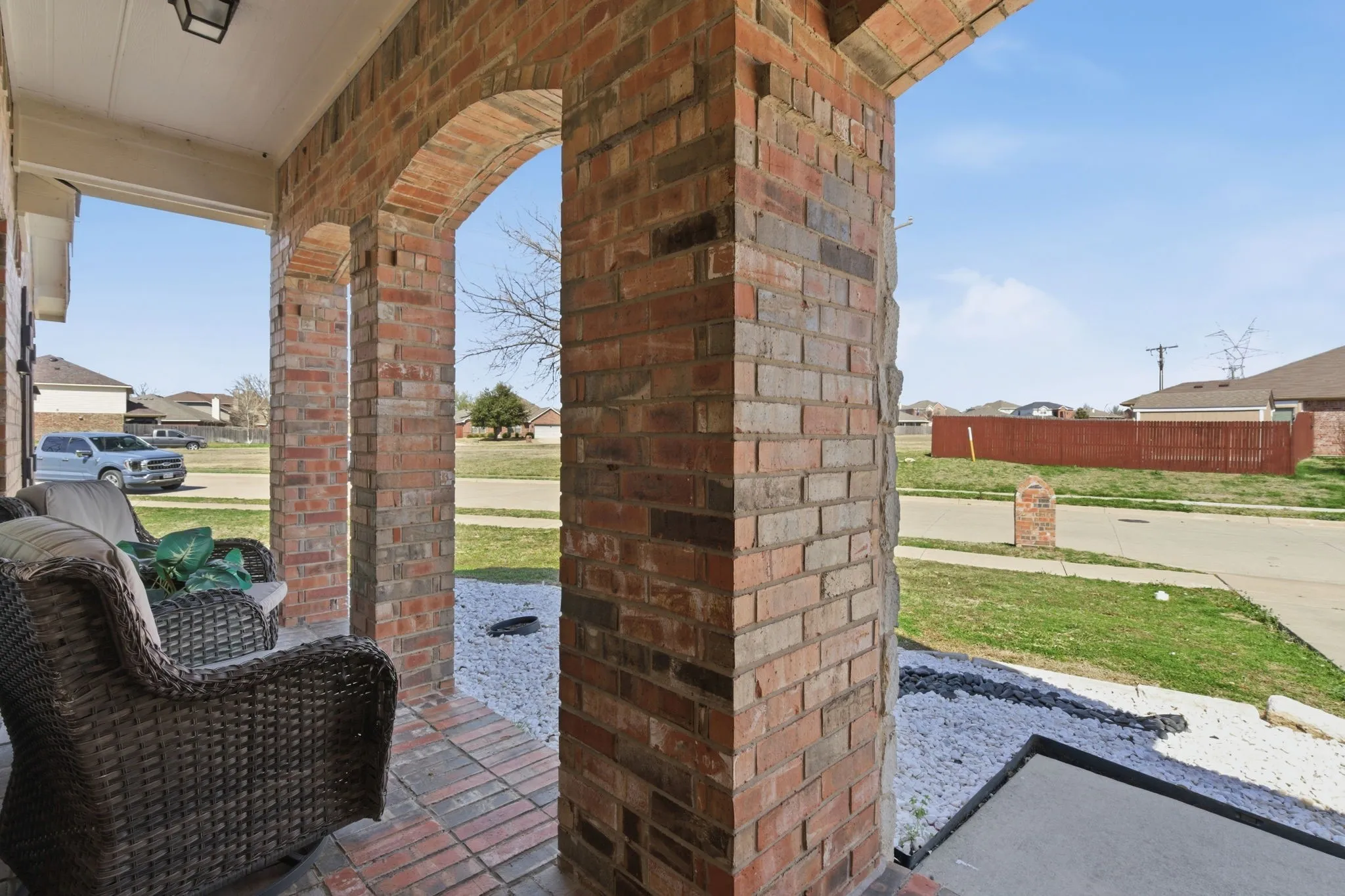 Covered front porch featuring brick columns, arched openings, a brick paver floor, and a porch light fixture