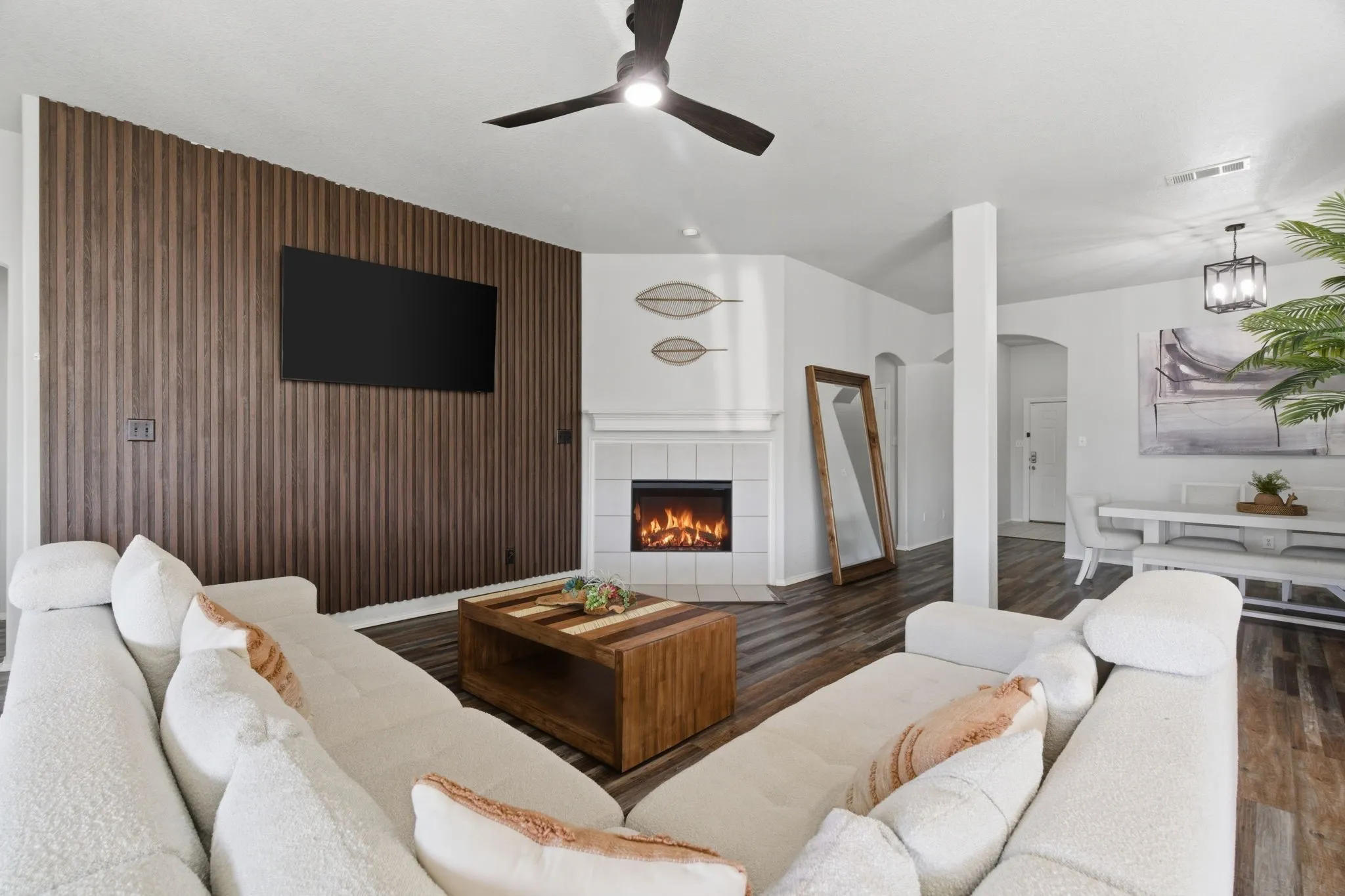 Living area featuring a floor-to-ceiling wood slat accent wall, a built-in fireplace with a tiled surround, wood-finish flooring, a ceiling fan, and recessed lighting