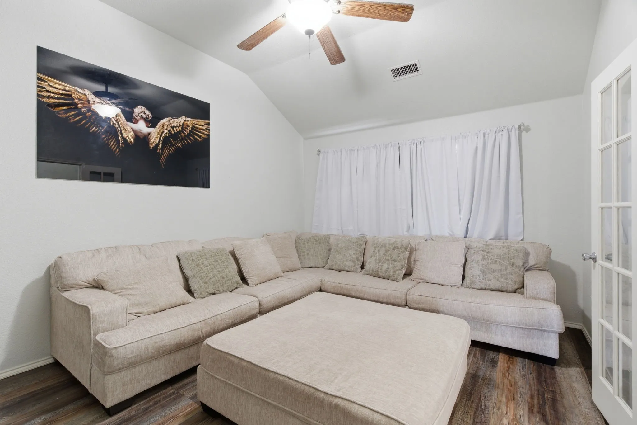 Living area featuring wood-finish flooring, a ceiling fan with light fixture, and a window with white drapes