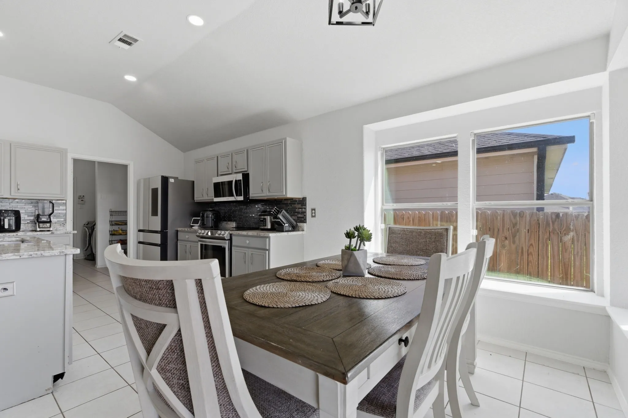 Vaulted ceiling kitchen featuring light gray cabinetry, stainless steel appliances, a dark tile backsplash, and a built-in window seat