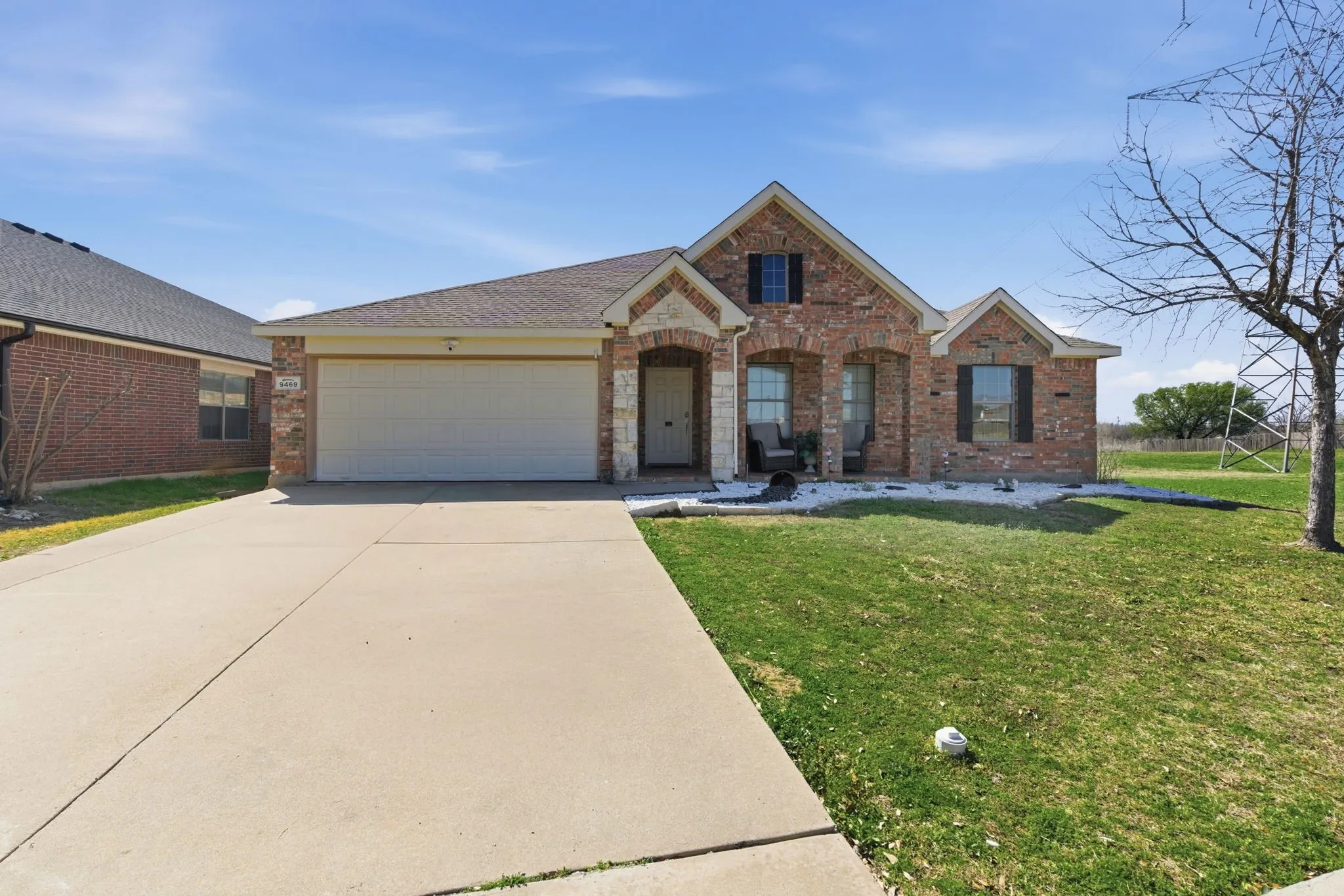 Brick and stone facade residence featuring a two-car garage, covered entry porch, and partial white rock landscaping