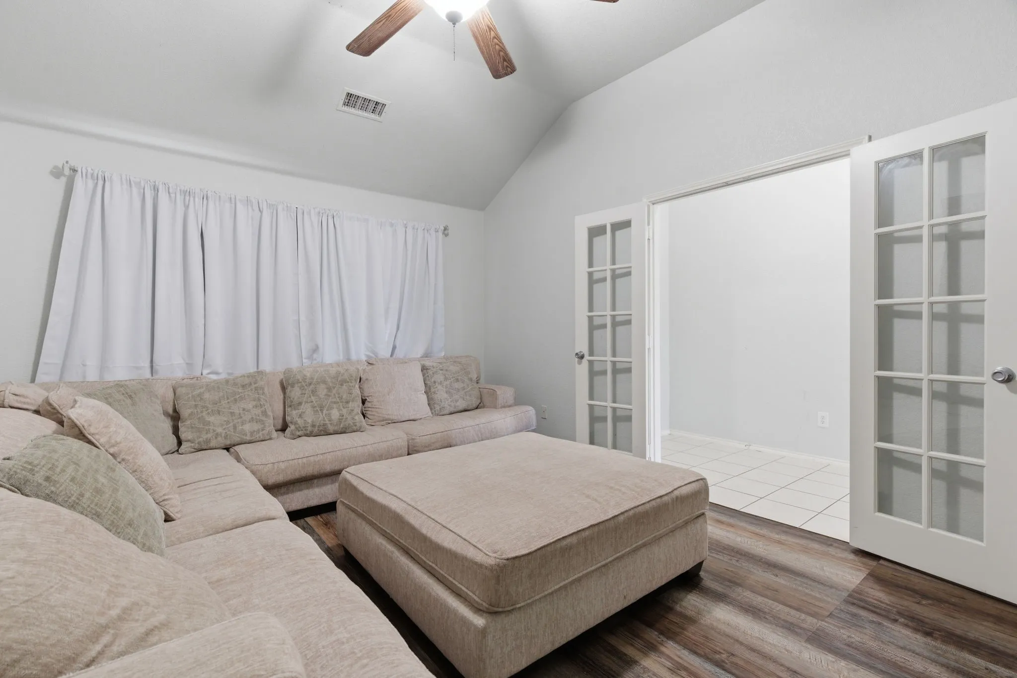 Living space featuring a vaulted ceiling with a ceiling fan, wood-finish flooring, and white walls