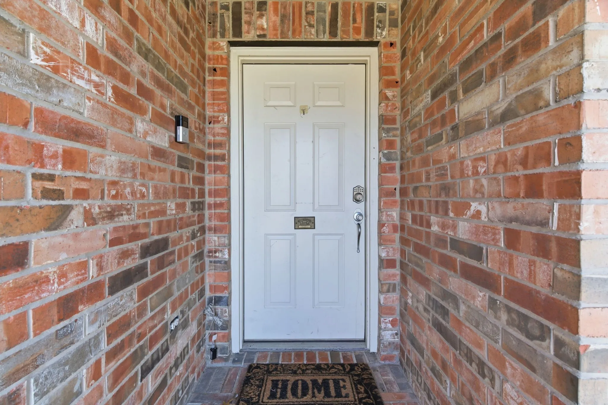 Front entry featuring a white paneled door with a mail slot, surrounded by a multi-toned brick facade