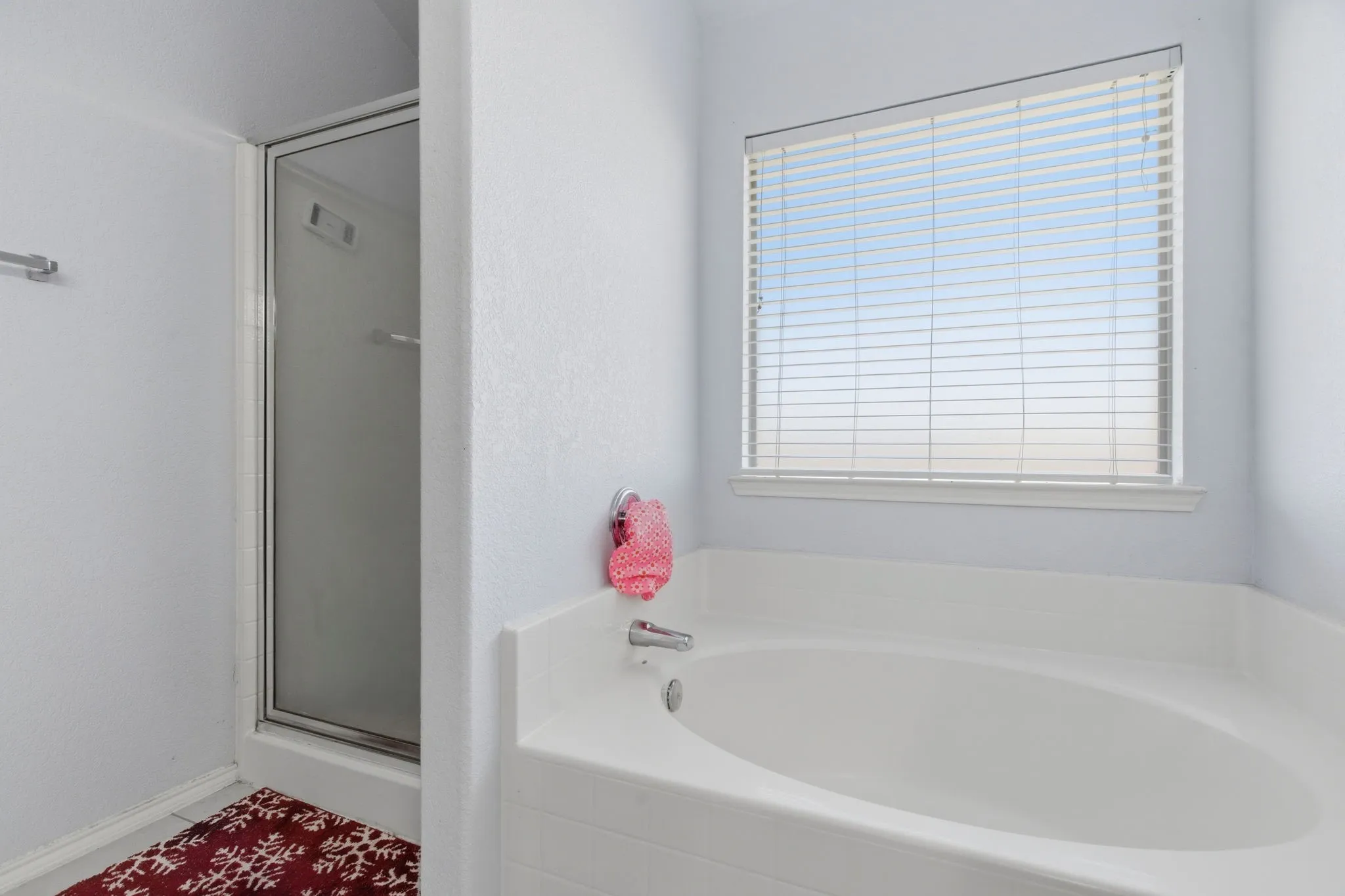 Bathroom featuring a built-in soaking tub with a silver-finish faucet, a window with horizontal blinds, and a glass-enclosed shower