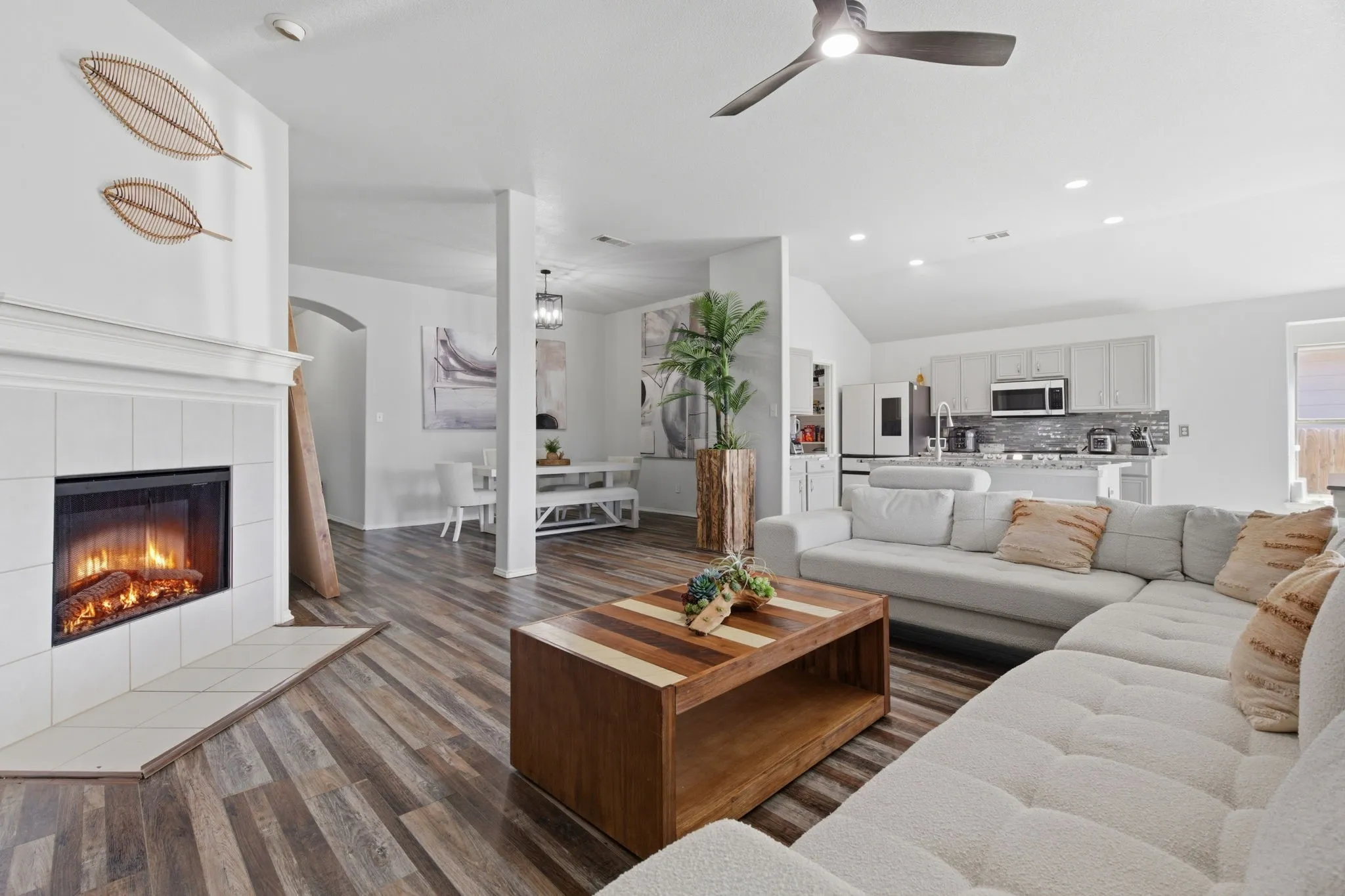Open-concept living space featuring wood-finish flooring, a white tiled fireplace, and a contemporary ceiling fan