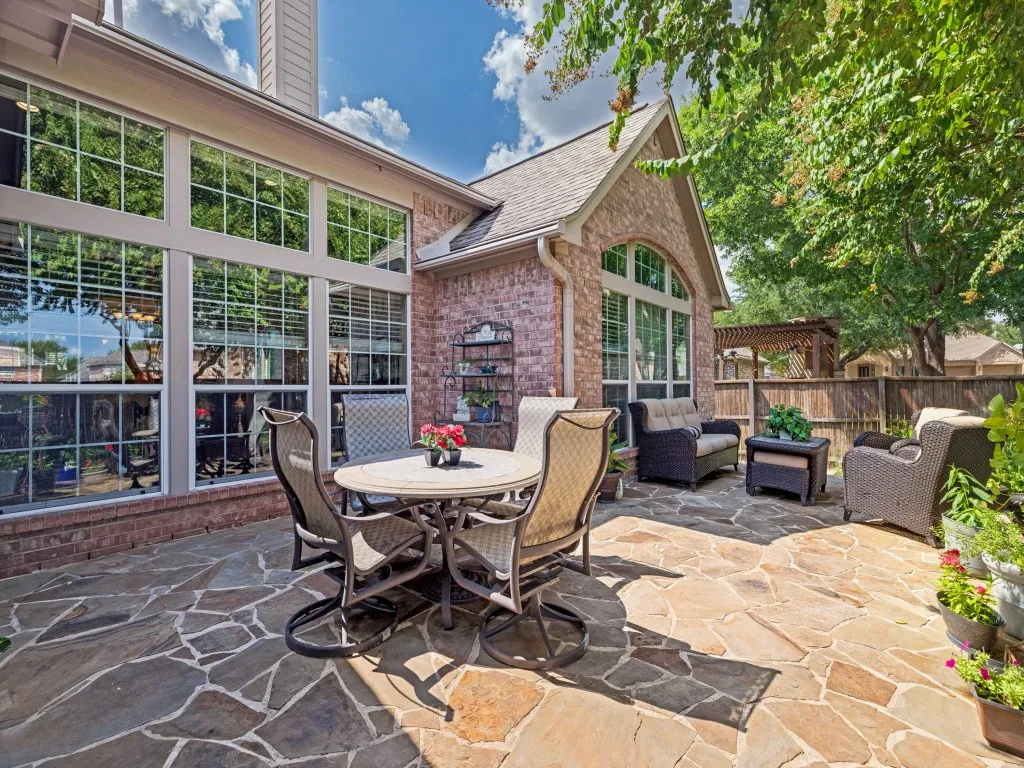 Expansive flagstone patio with a brick exterior, large picture windows, and a wood privacy fence