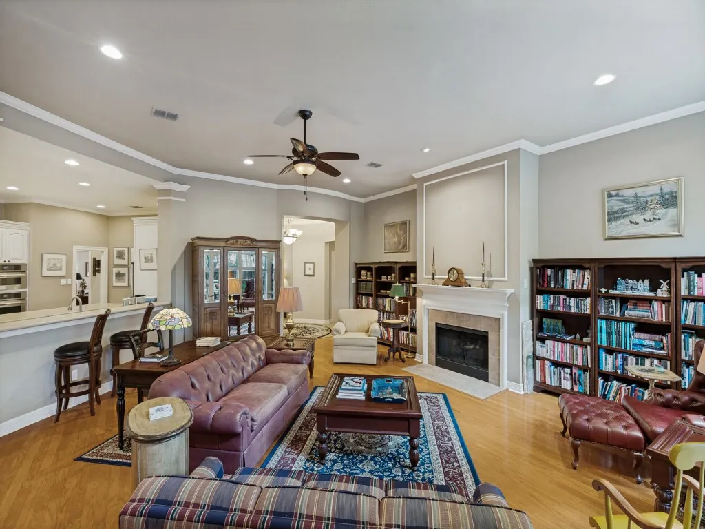 Hardwood-style flooring throughout, built-in shelving, fireplace with stone surround, recessed lighting, and a ceiling fan