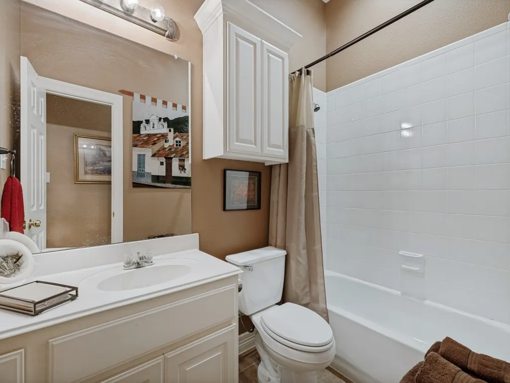 White vanity with integrated sink, white upper cabinetry, full-width mirror, white bathtub with tile surround, and neutral wall color