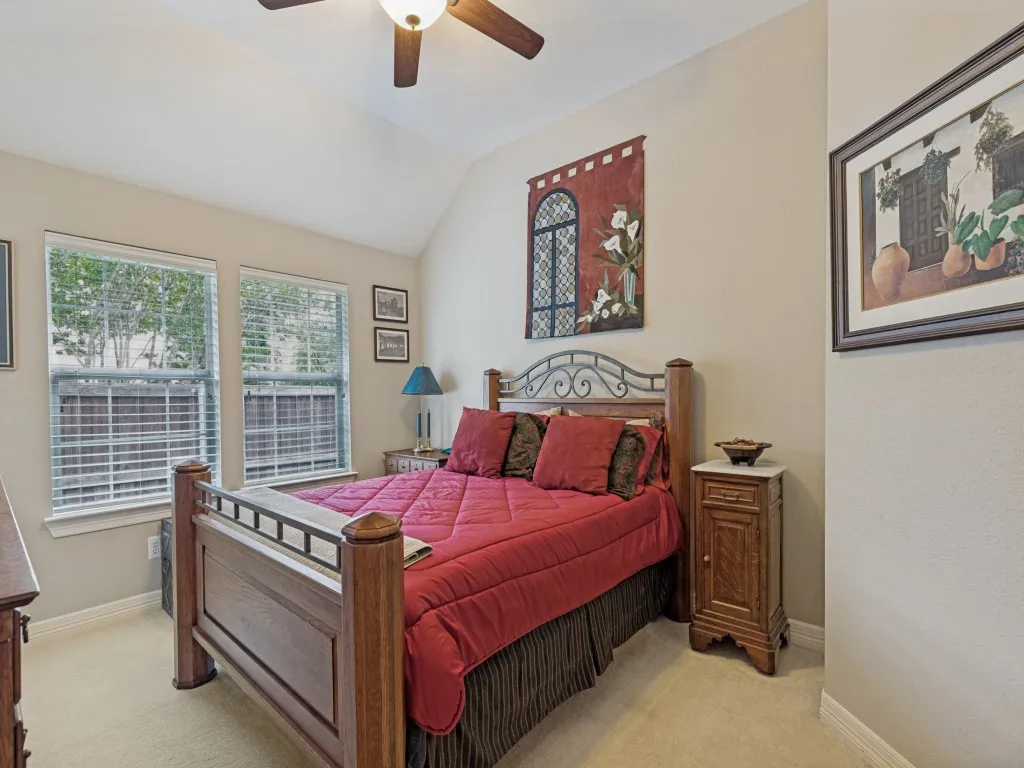 Vaulted ceiling with a ceiling fan, two windows, carpet flooring, and neutral wall paint