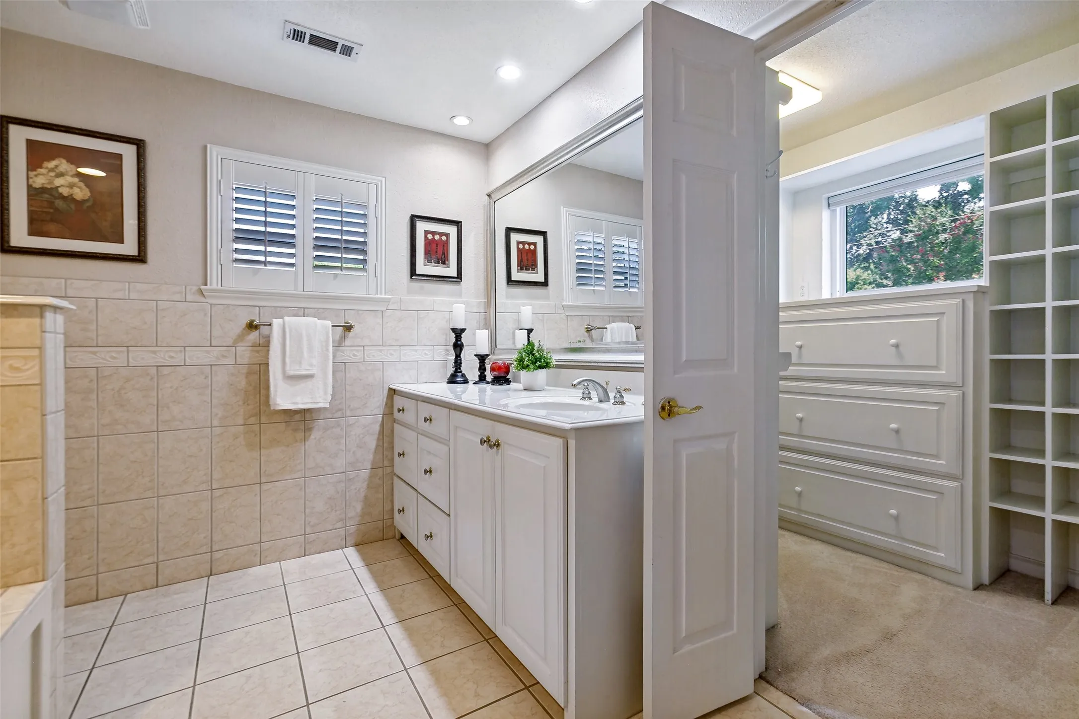  Tile flooring, white vanity with great storage, plantation shutters and a view of the closet.