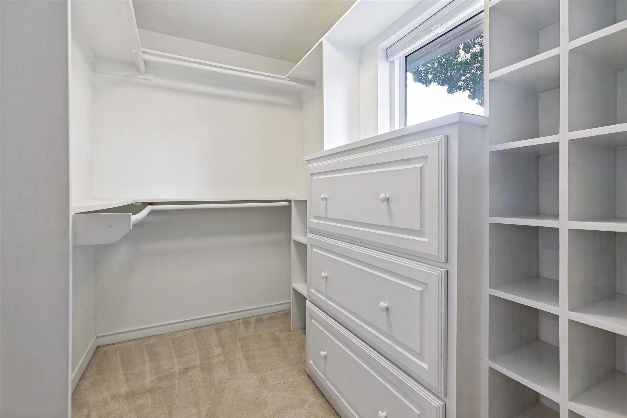 Custom walk-in closet featuring deep drawers, grid shelving, 3 walls of rods, and a window for natural light