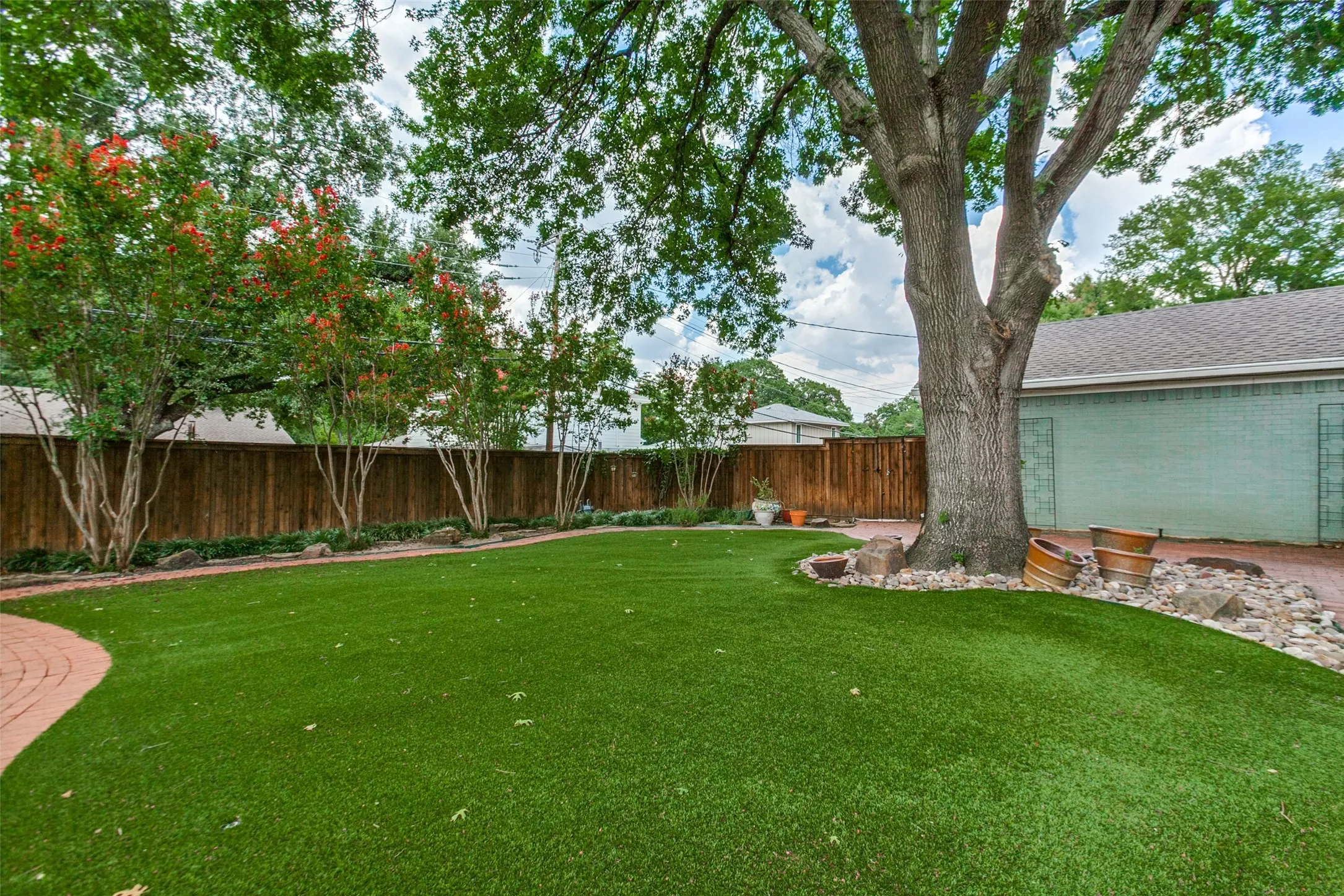 Expansive backyard featuring mature trees, a red brick patio, and a wood privacy fence