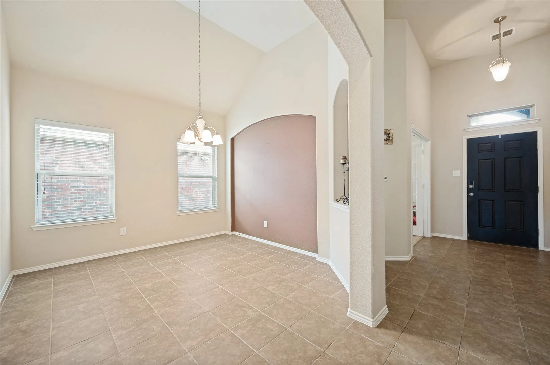 Vaulted ceiling dining area featuring tile flooring, a multi-light chandelier, and two windows with blinds
