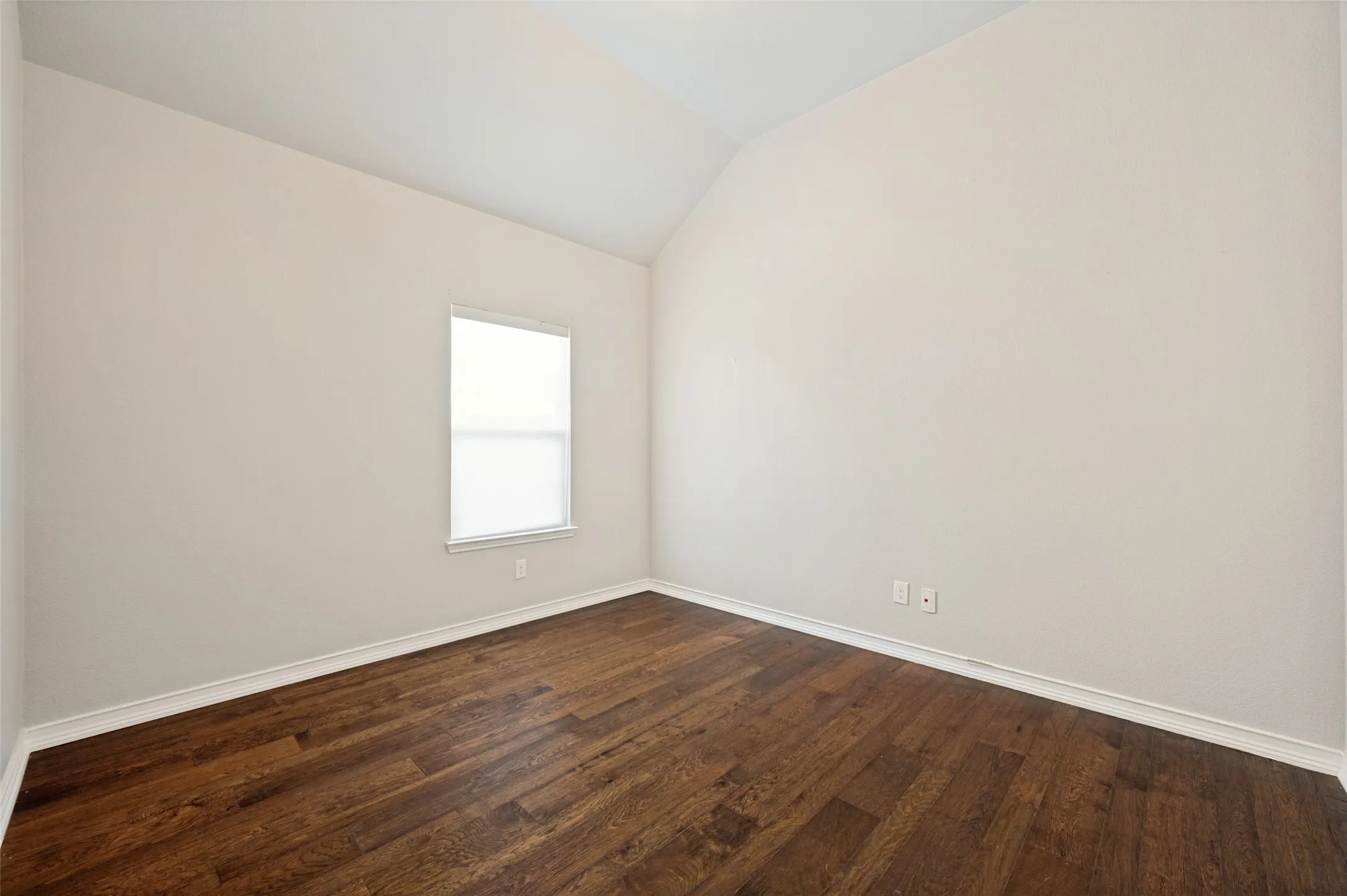 Room featuring wood-finish flooring, light neutral wall tones, and a vaulted ceiling