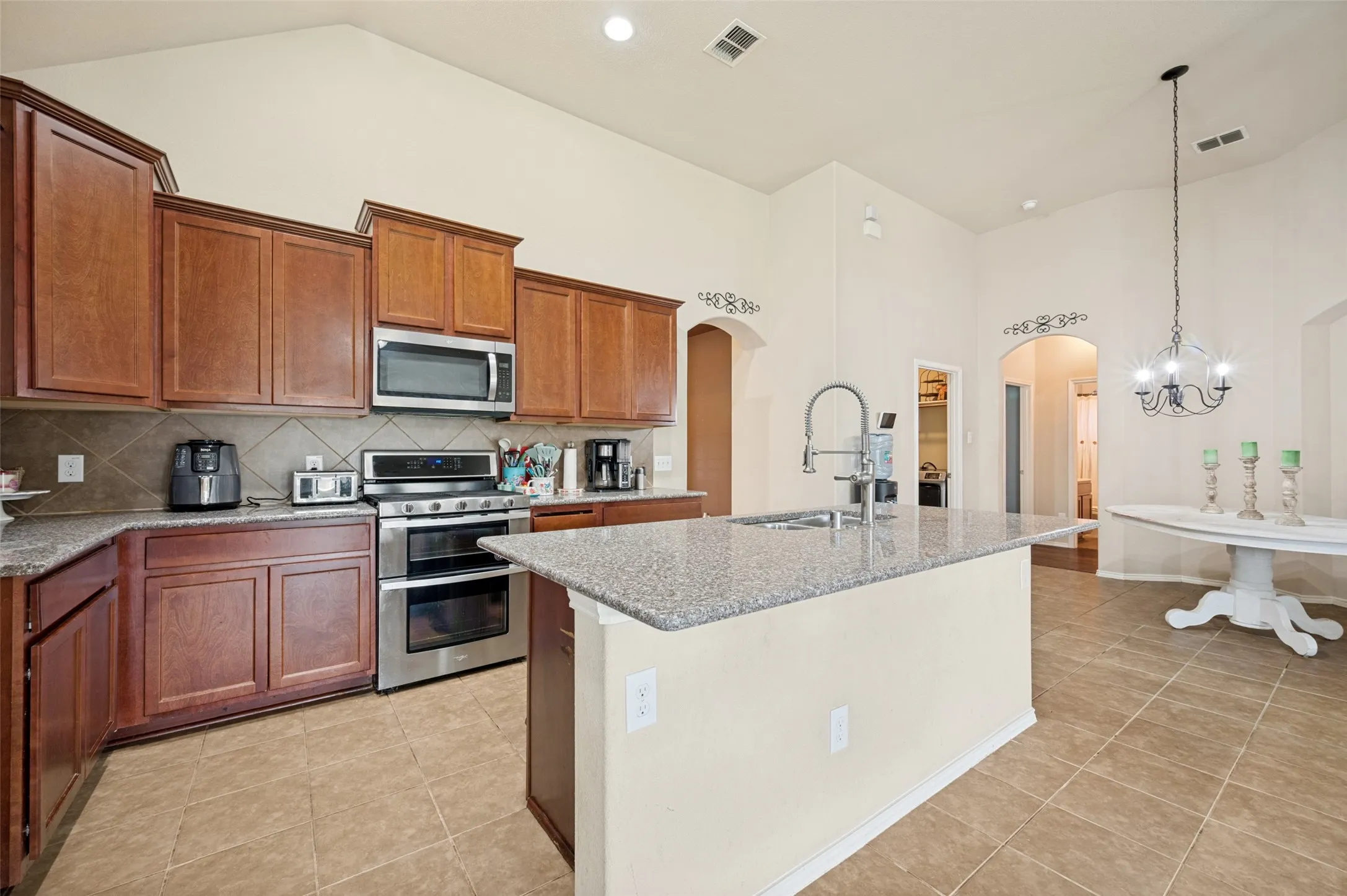Kitchen featuring wood cabinetry, stainless steel appliances, granite countertops, and an island with an integrated sink