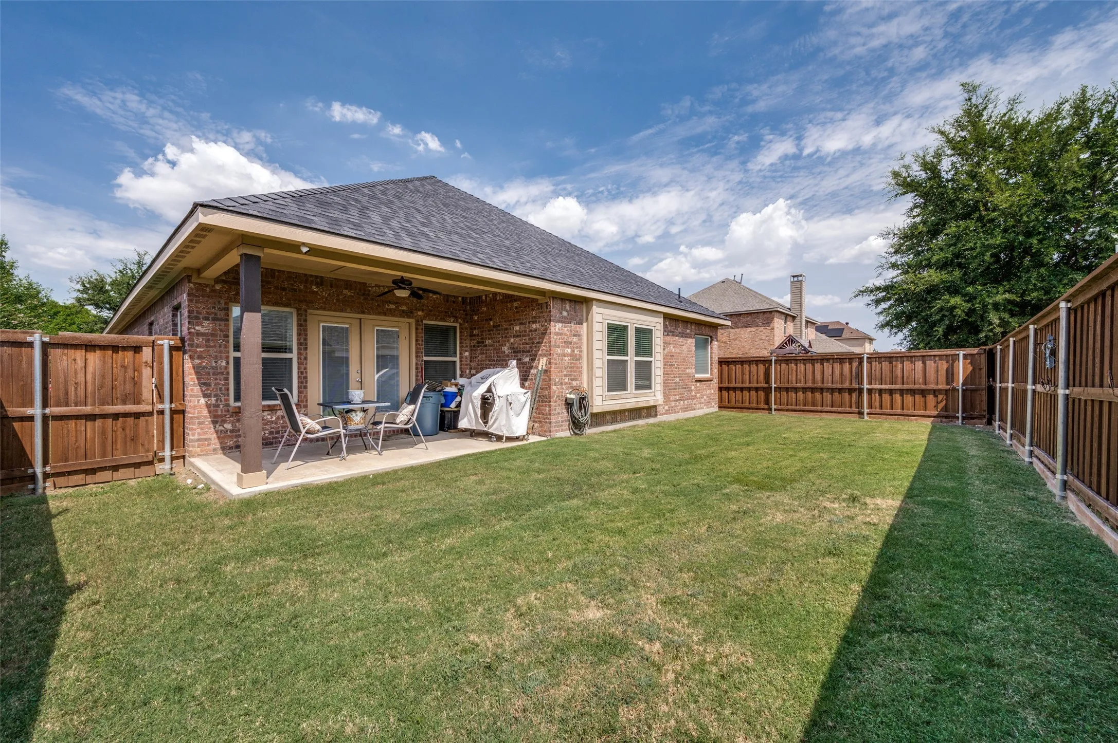 Spacious backyard featuring a covered patio with a ceiling fan, brick exterior, wood privacy fencing, and a manicured lawn