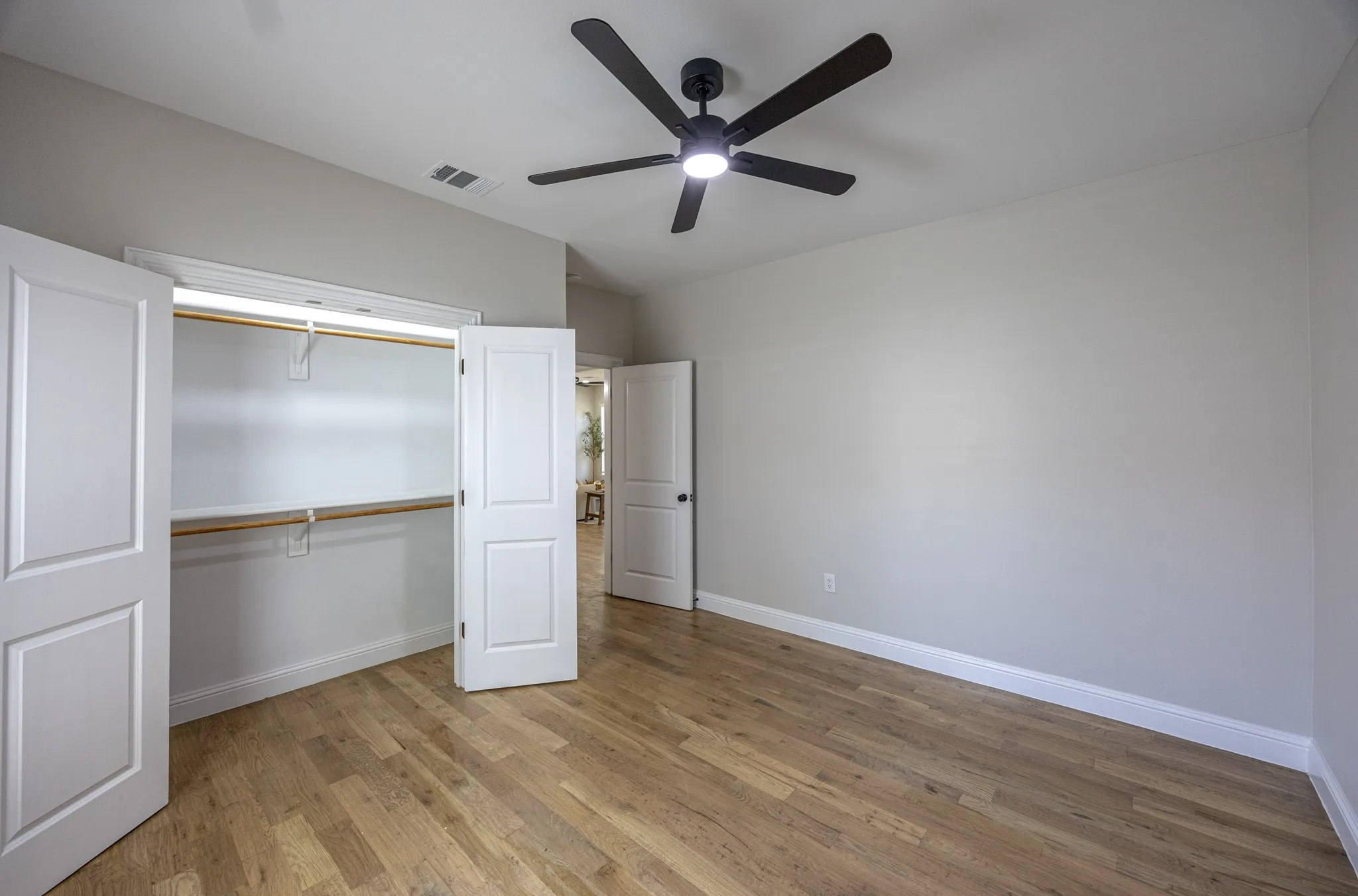 Spacious room featuring wood-finish flooring, light grey walls, and a contemporary black ceiling fan with integrated lighting