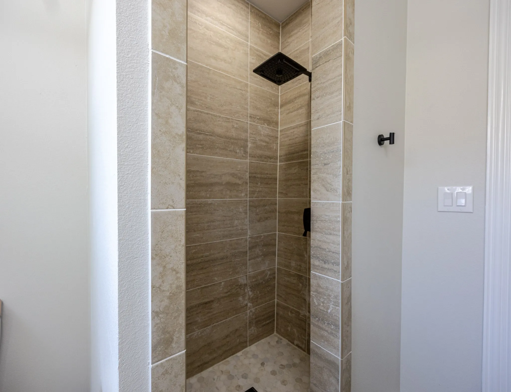 Walk-in shower featuring stacked rectangular wall tiles, a hexagonal floor tile pattern, and matte black fixtures