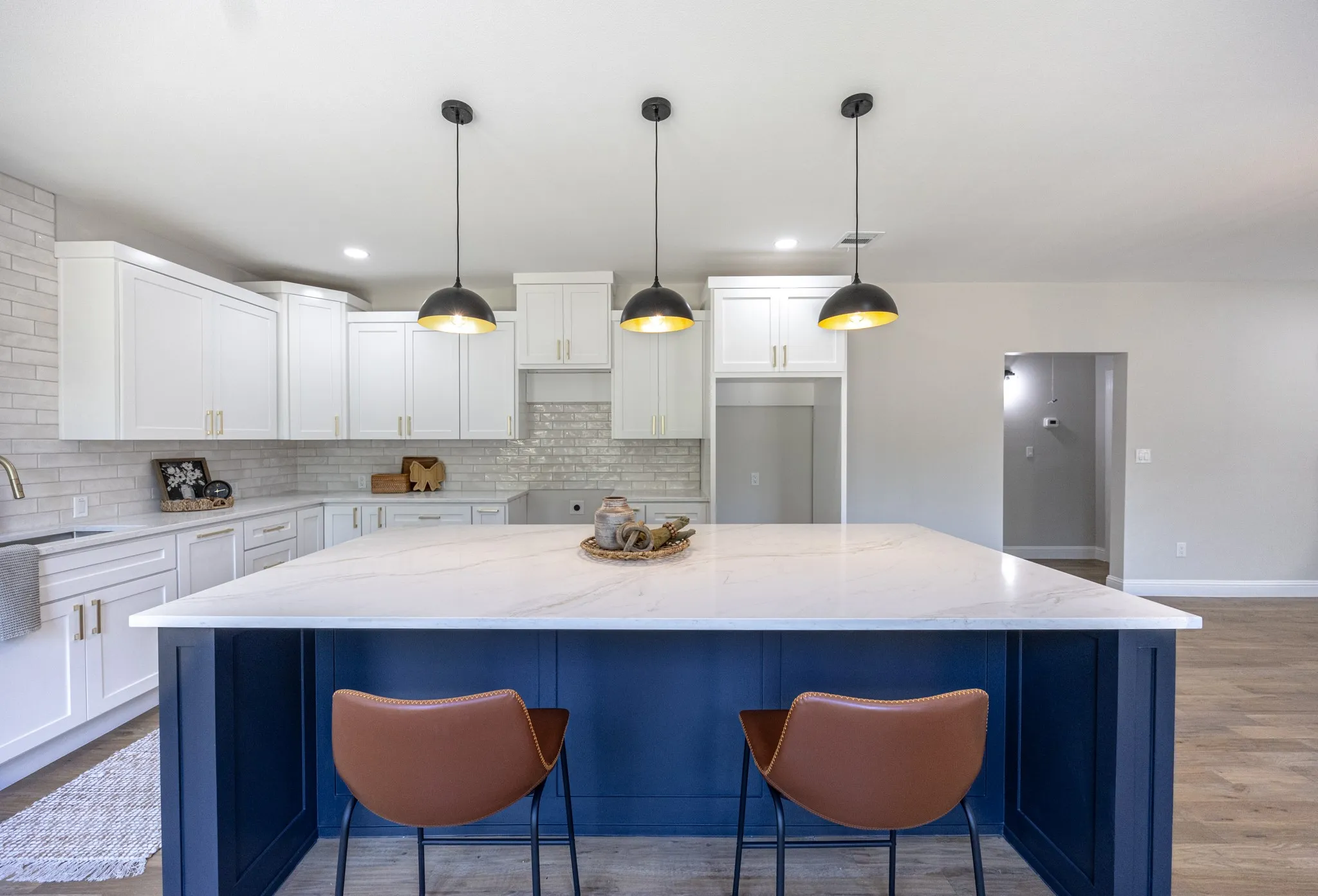 Spacious kitchen featuring a large central island with a white countertop and blue base, white cabinetry, a white subway tile backsplash, and wood-finish flooring