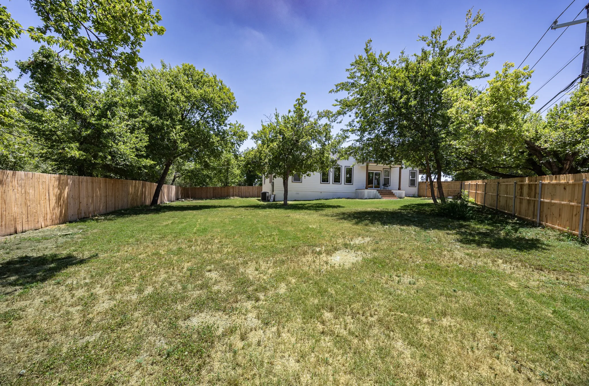 Expansive backyard featuring a natural grass lawn, mature trees, and a full privacy fence
