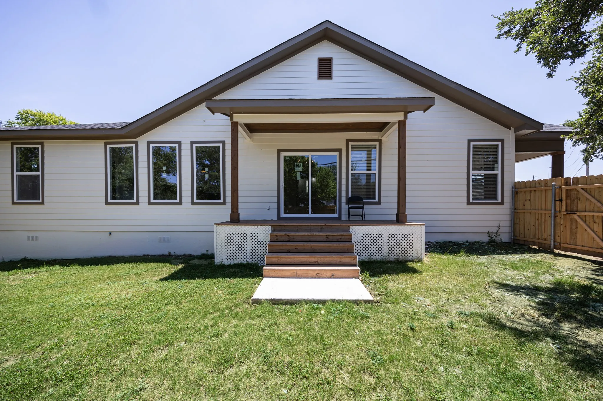 Rear exterior featuring a covered wood-finish deck with wooden posts, white lattice skirting, and sliding glass doors