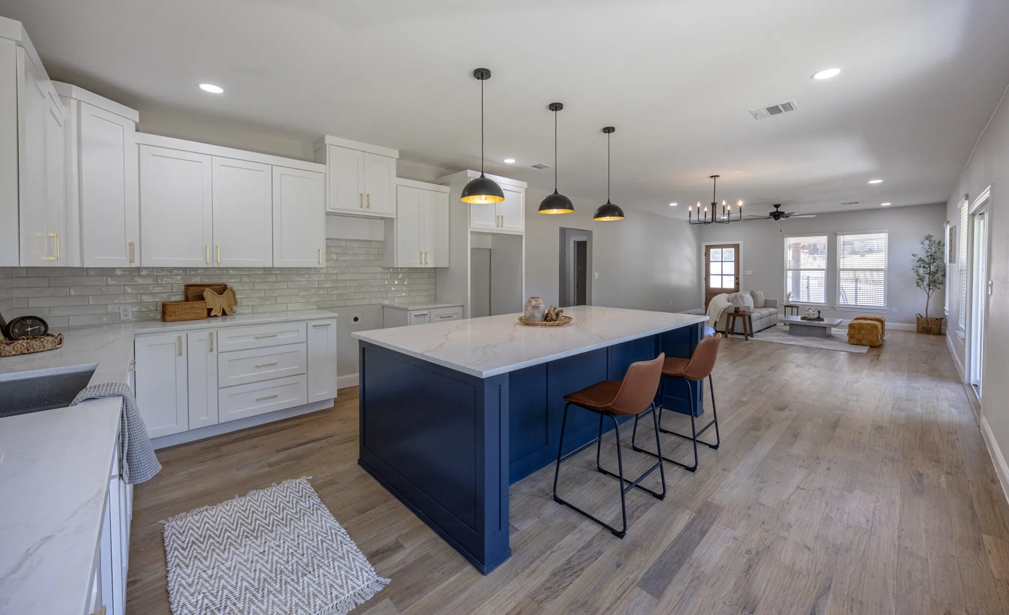 Open-concept kitchen featuring a navy island with a light-toned countertop, white cabinetry with gold-tone hardware, and wood-finish flooring