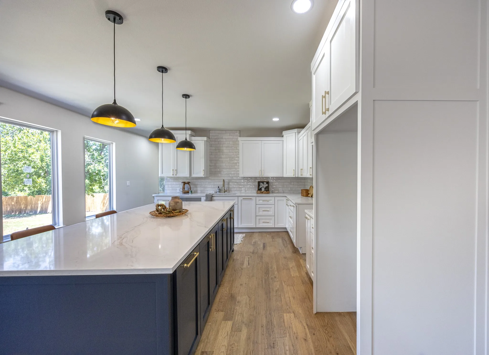 Spacious kitchen featuring a large central island with a light-toned countertop, white shaker-style cabinetry, a white brick-patterned backsplash, and wood-finish flooring