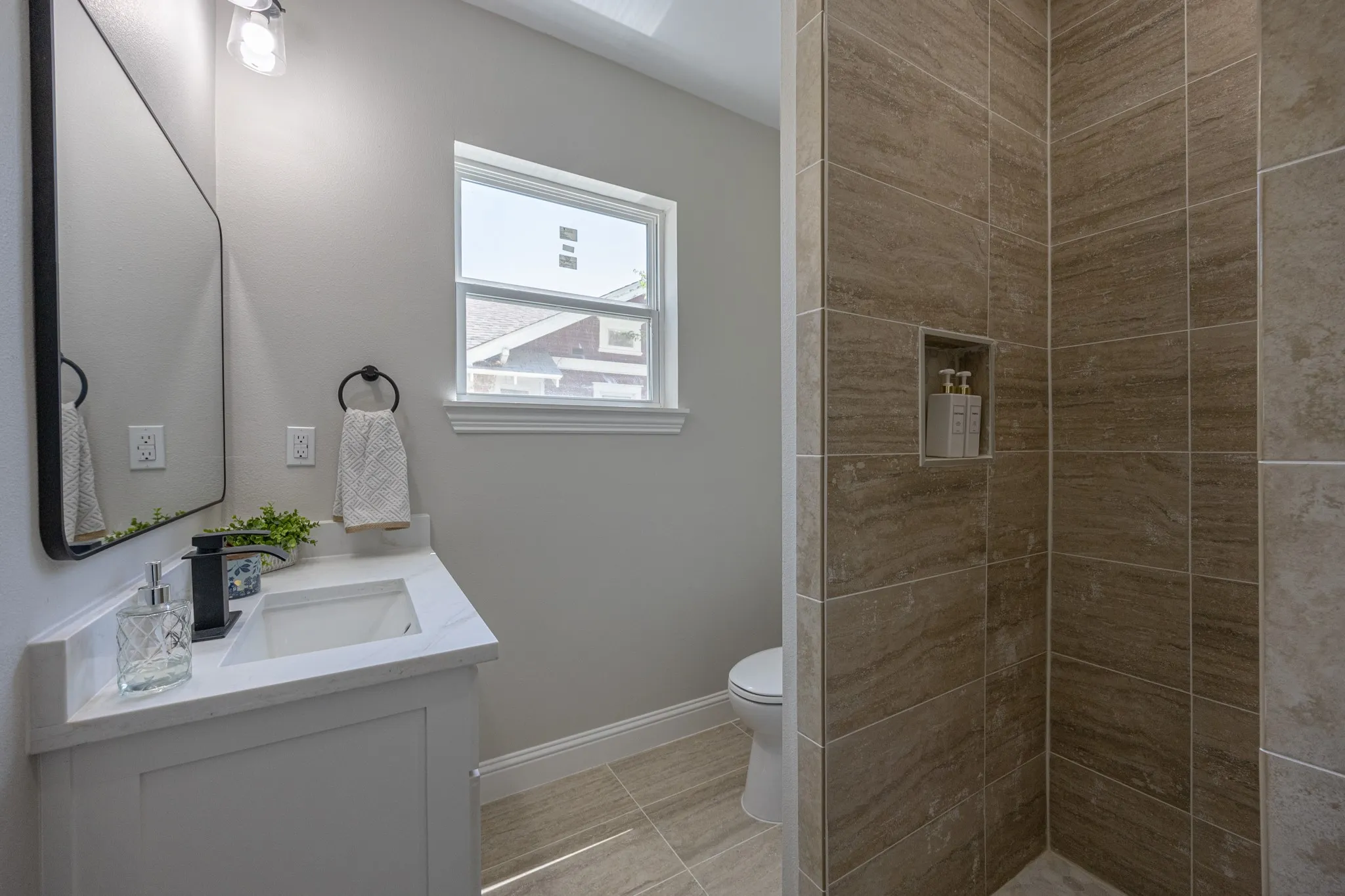 Contemporary bathroom featuring a white vanity with integrated sink, a rectangular black-framed mirror, and a walk-in shower with large format tile and a recessed niche