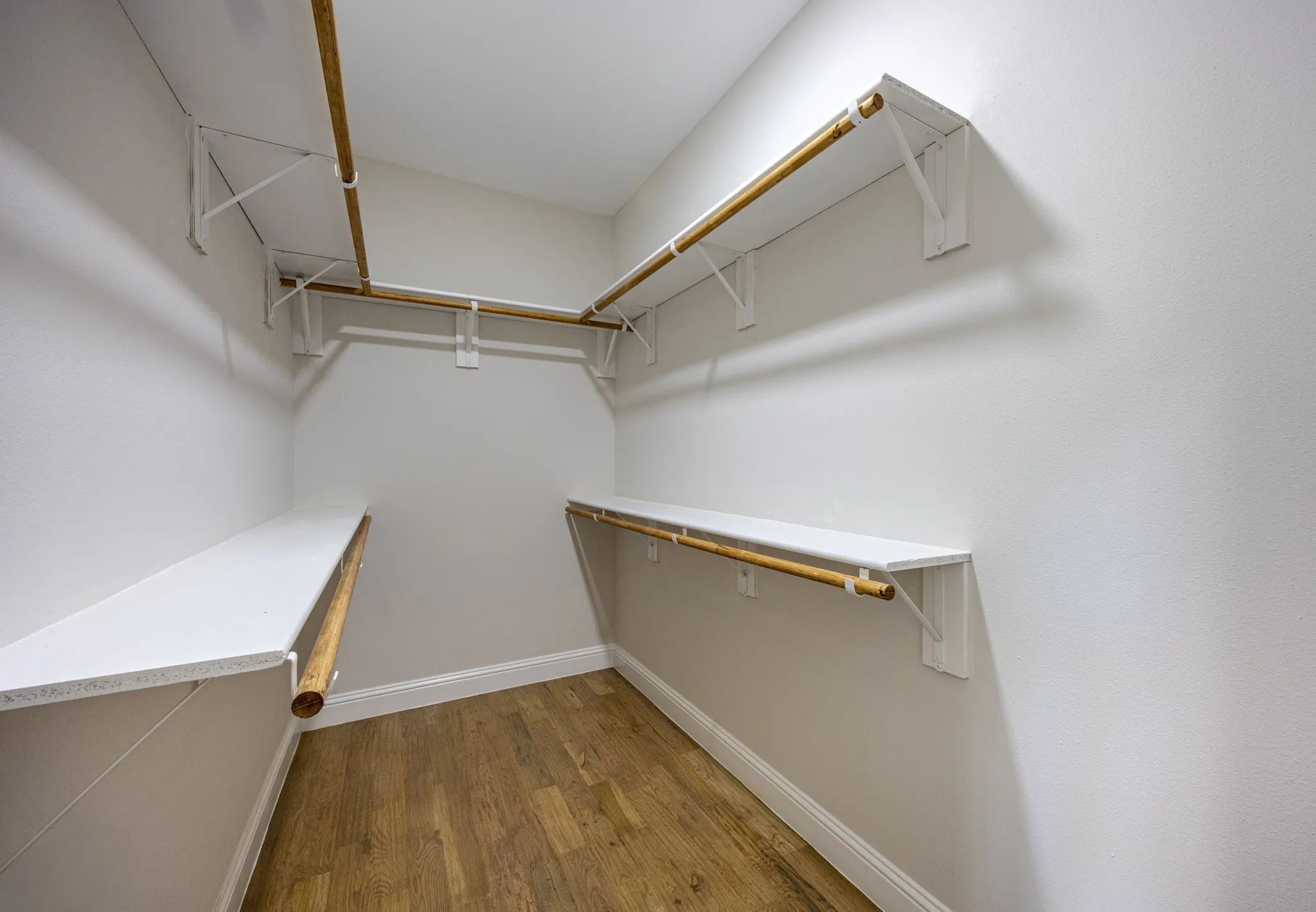 Walk-in closet featuring white walls, wood-finish flooring, and multiple built-in shelves with hanging rods